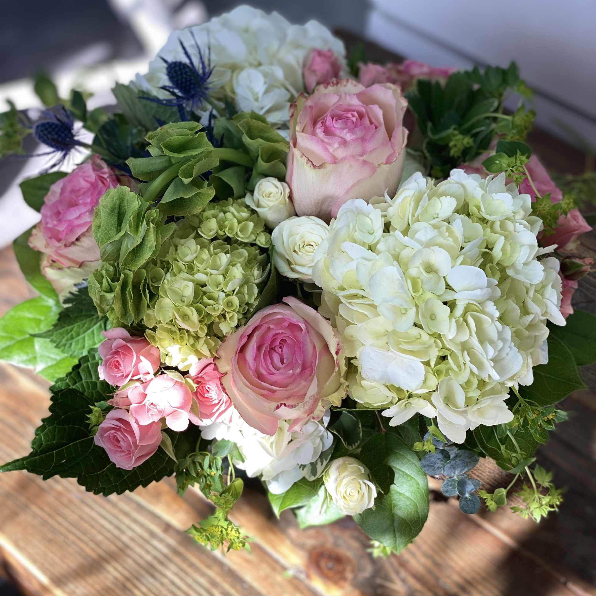 Round arrangement of pink roses with white and green hydrangeas in a low glass vase