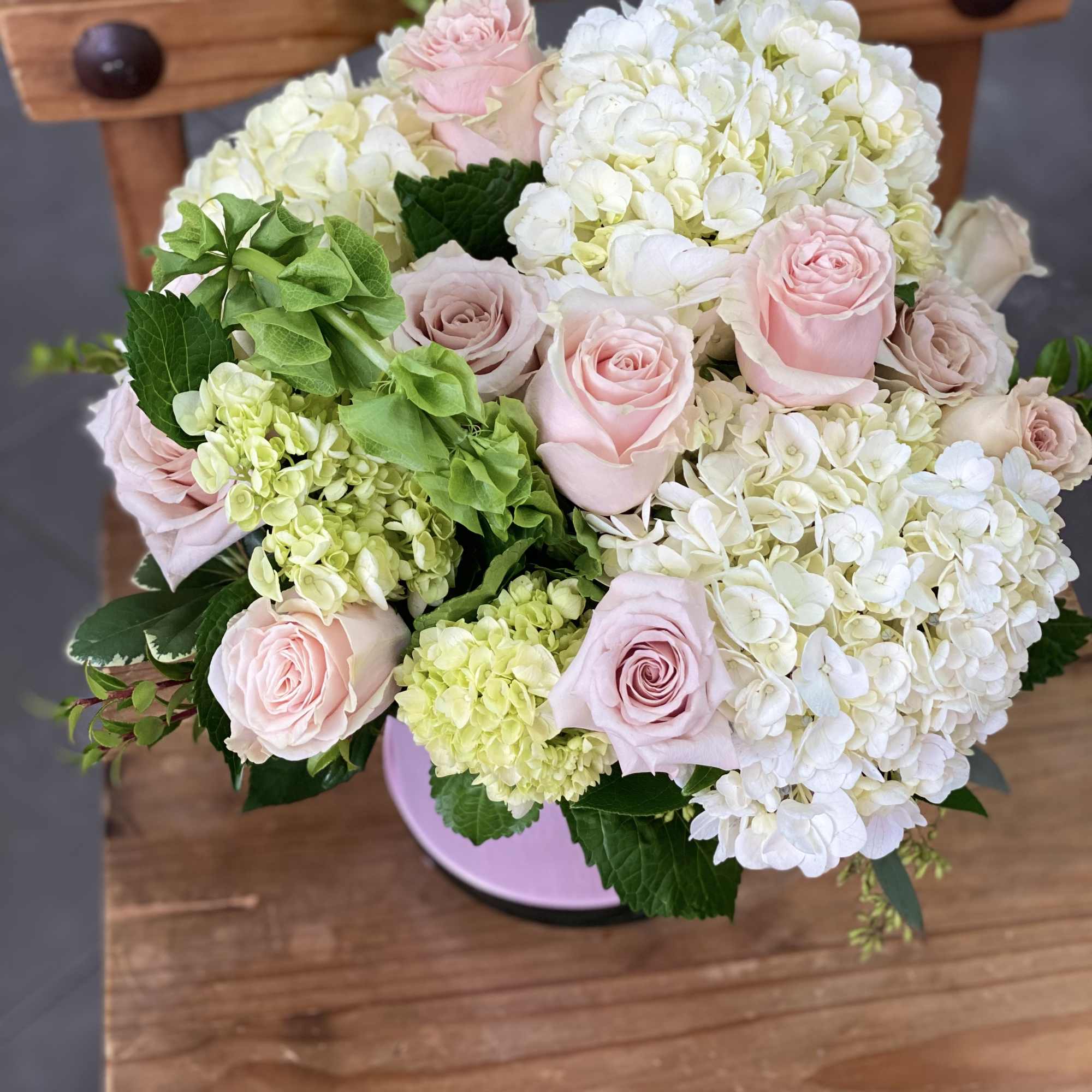 Cylinder vase wrapped with pink ribbon, filled with hydrangeas and a dozen