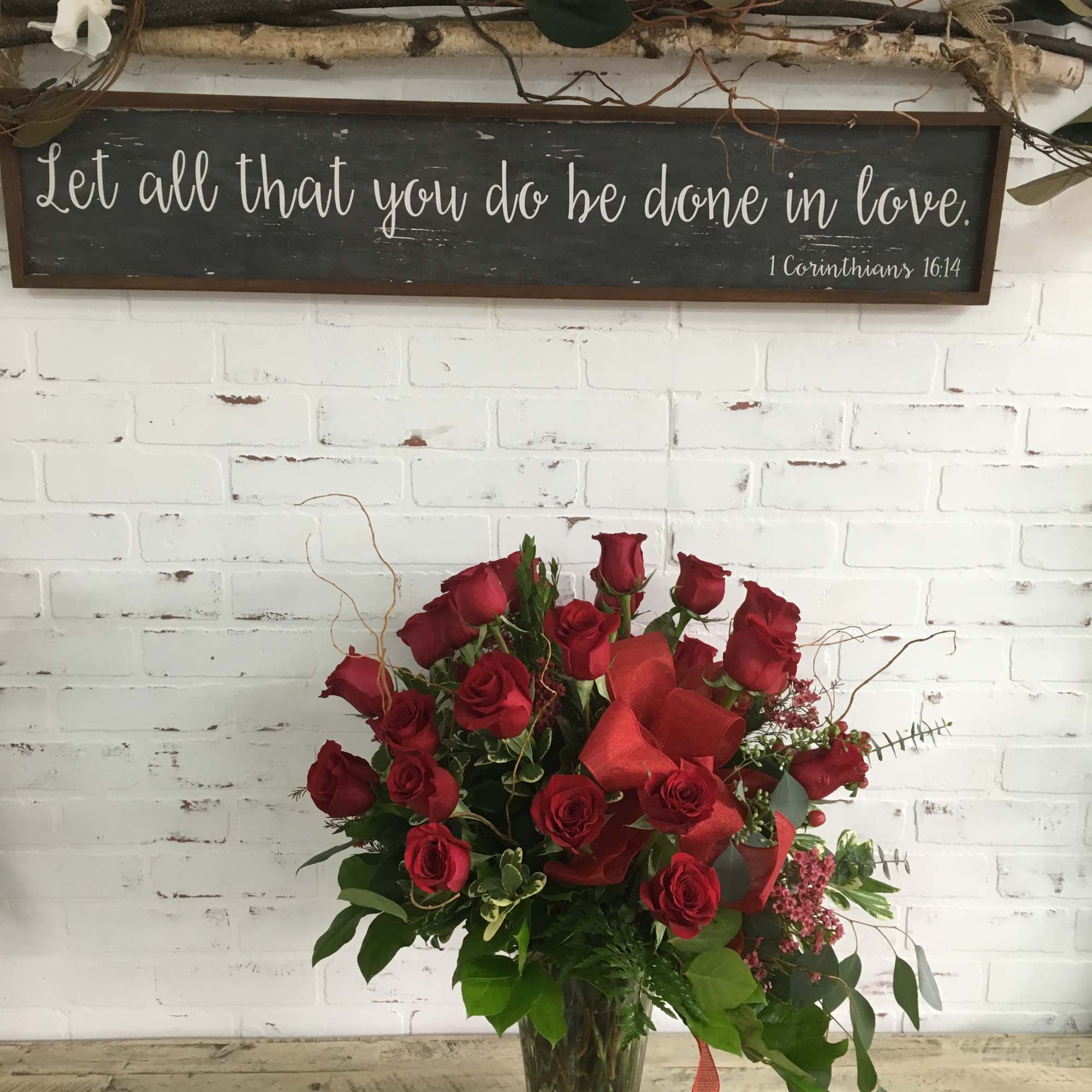 Red rose arrangement in a glass vase with greenery and ribbon