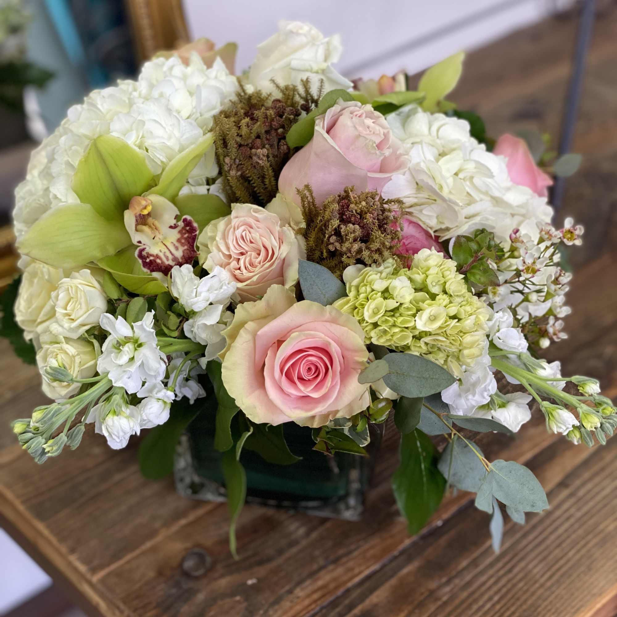 Low arrangement of pink roses, white hydrangeas, and a green cymbidium orchid in a glass cube vase