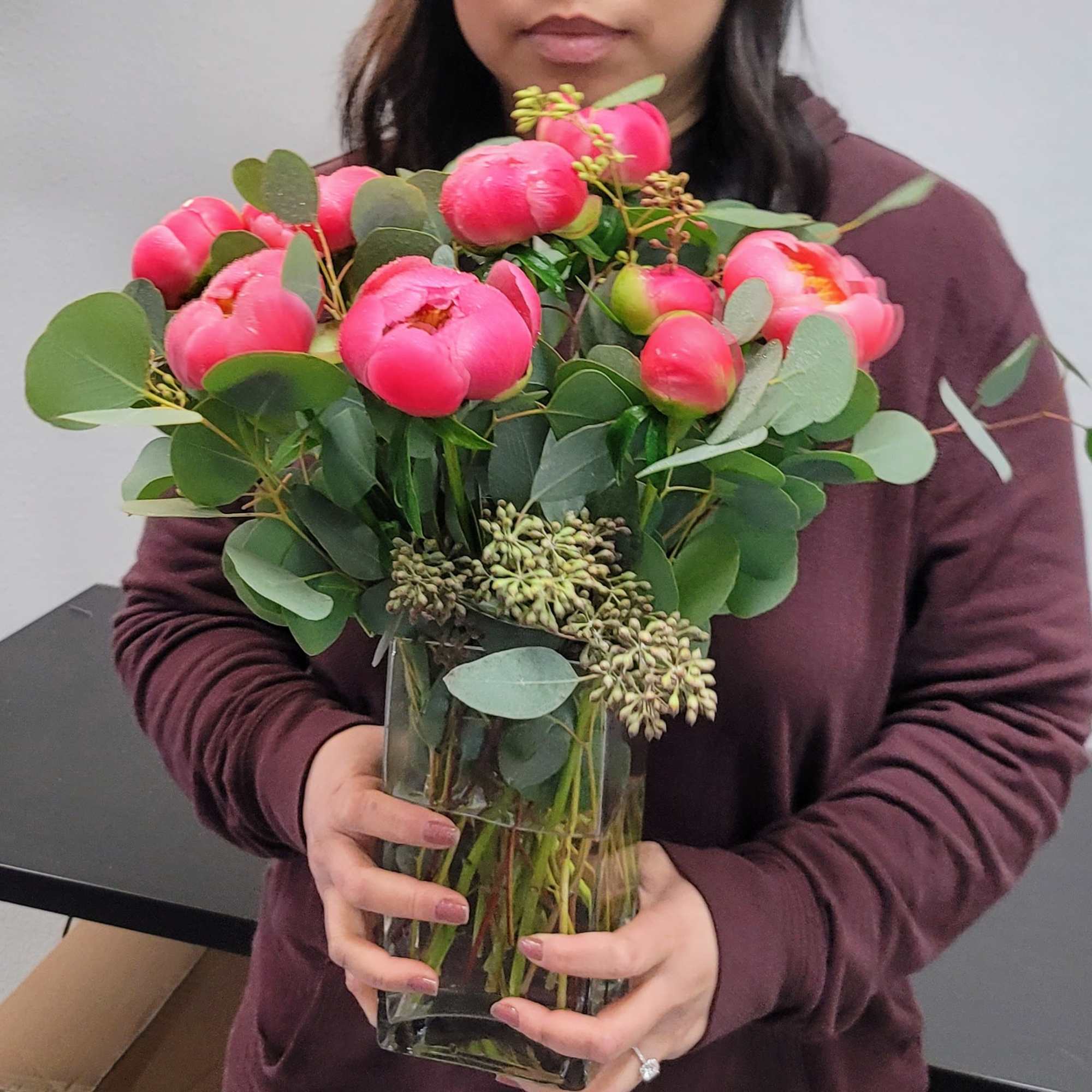 Person holding a vase of bright pink peonies with eucalyptus
