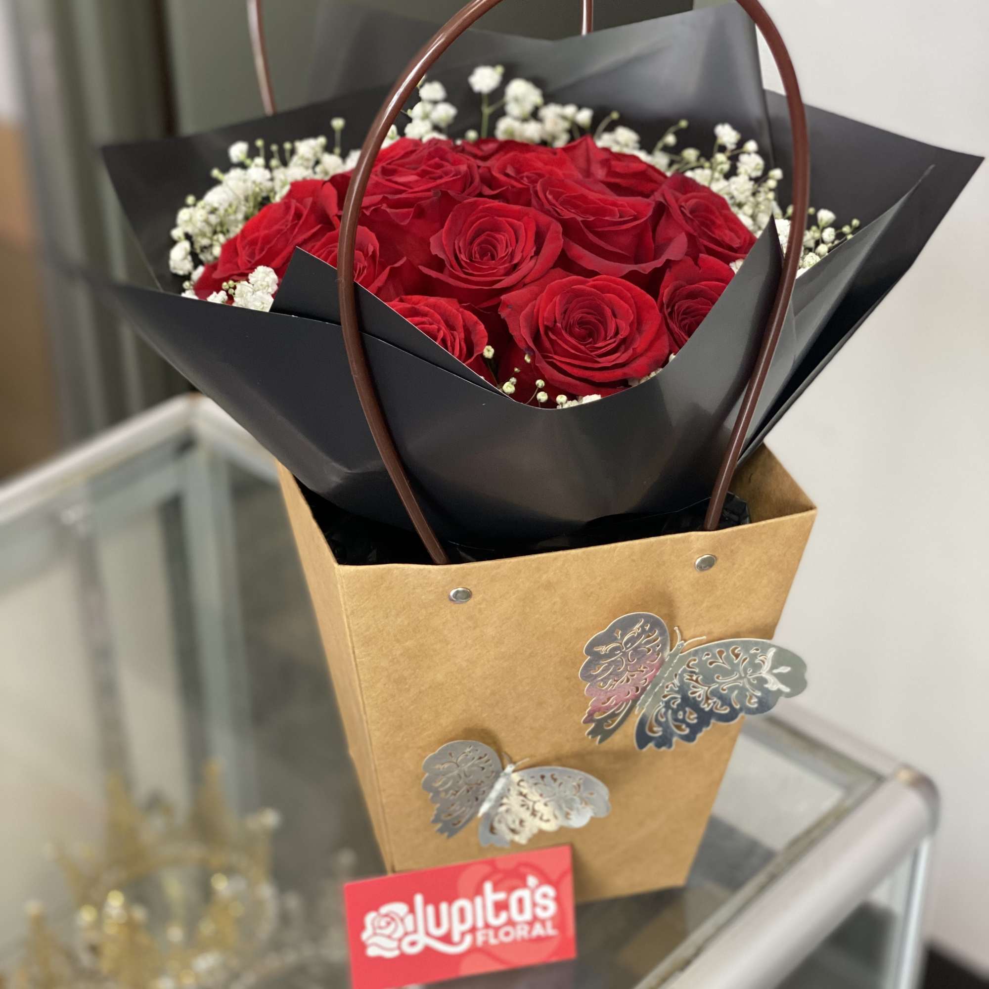 Bouquet of red roses with white baby's breath in black wrap and a kraft gift bag