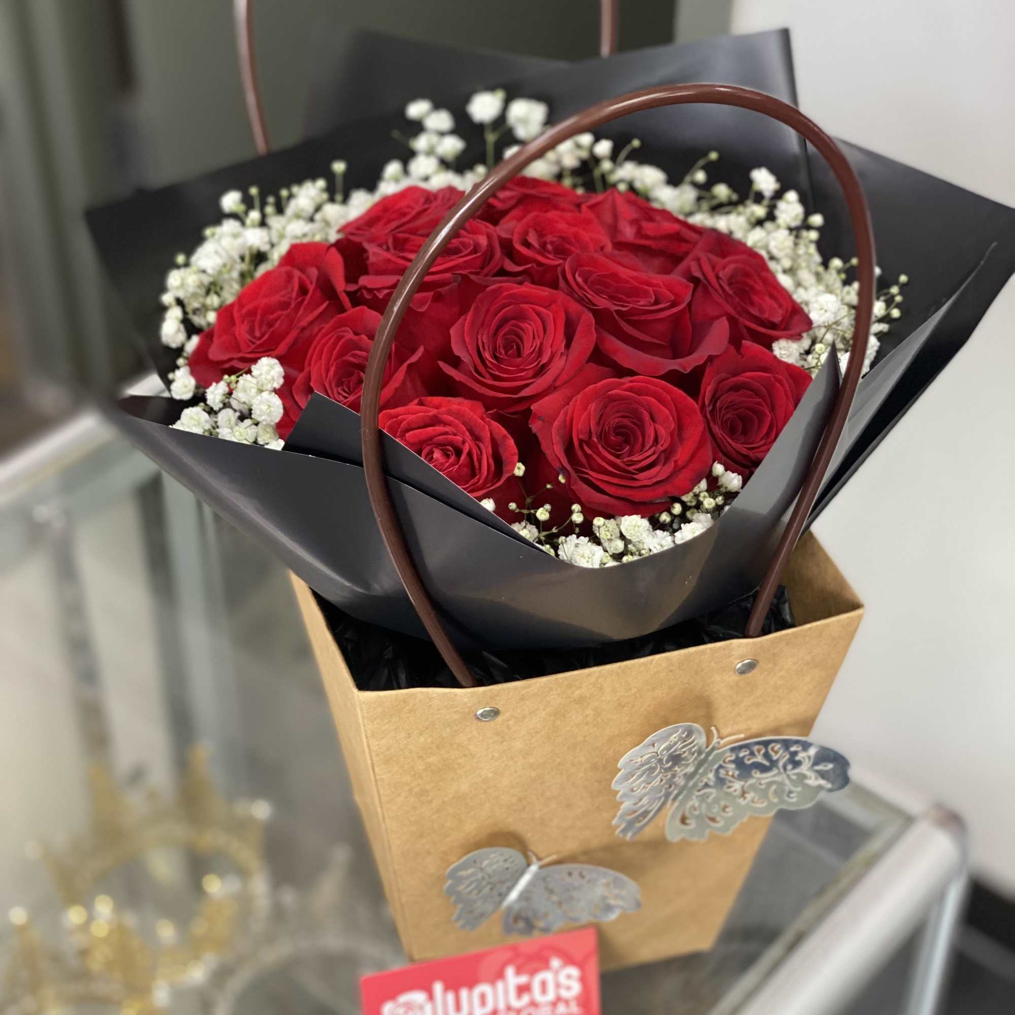 Bouquet of red roses with white baby's breath in a black wrap and brown gift bag