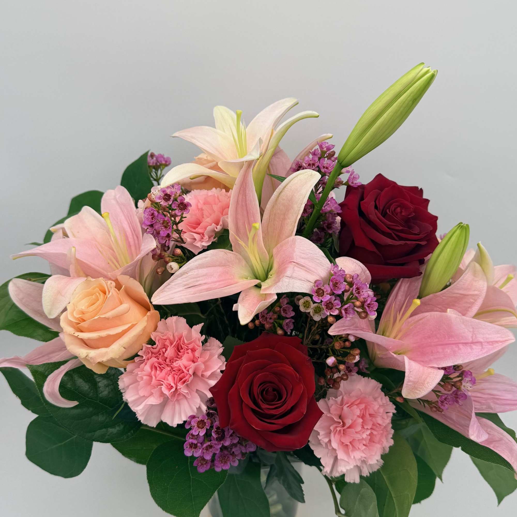 Bouquet of pink lilies, red and peach roses, and pink carnations in a vase