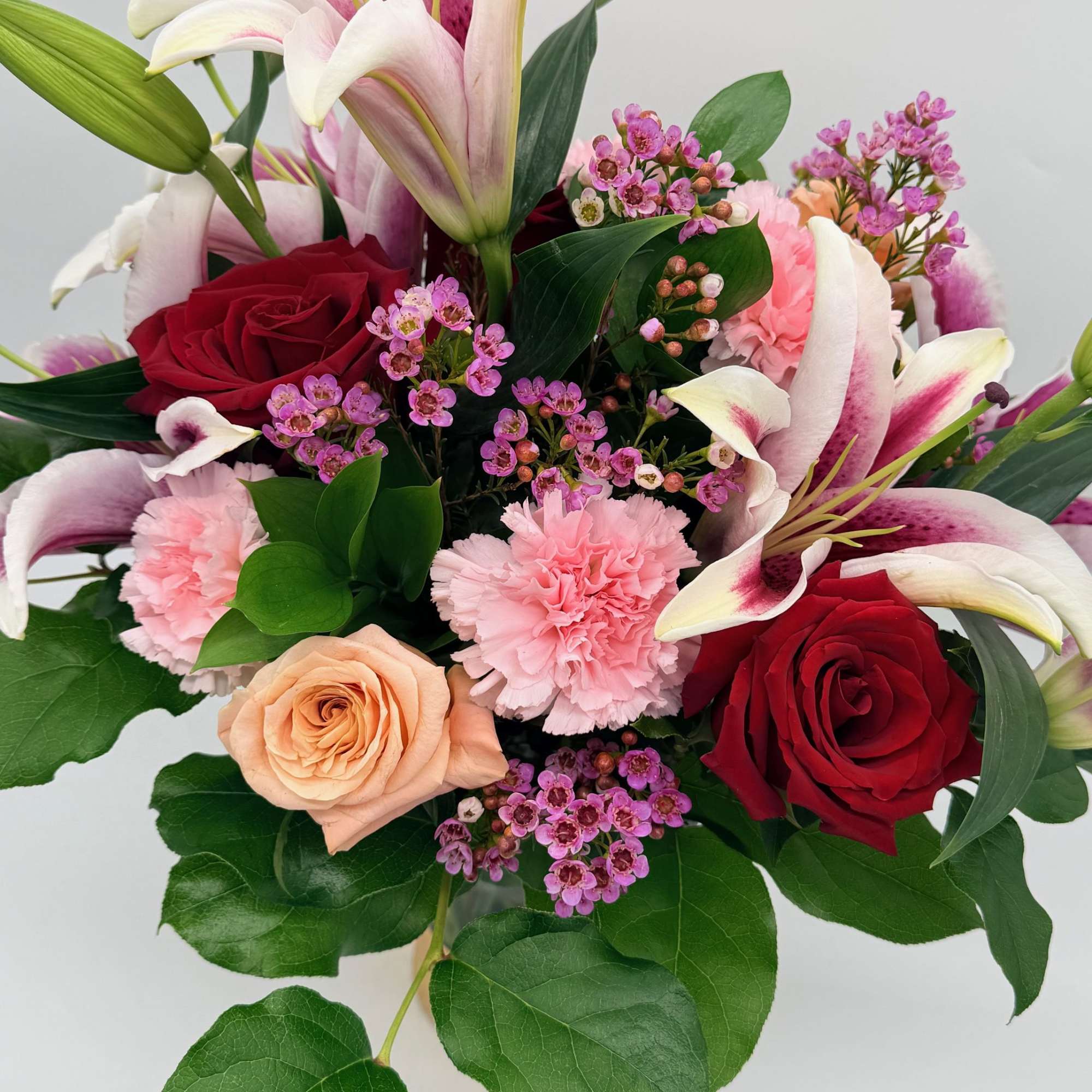 Bouquet of pink lilies, red roses, and carnations with greenery