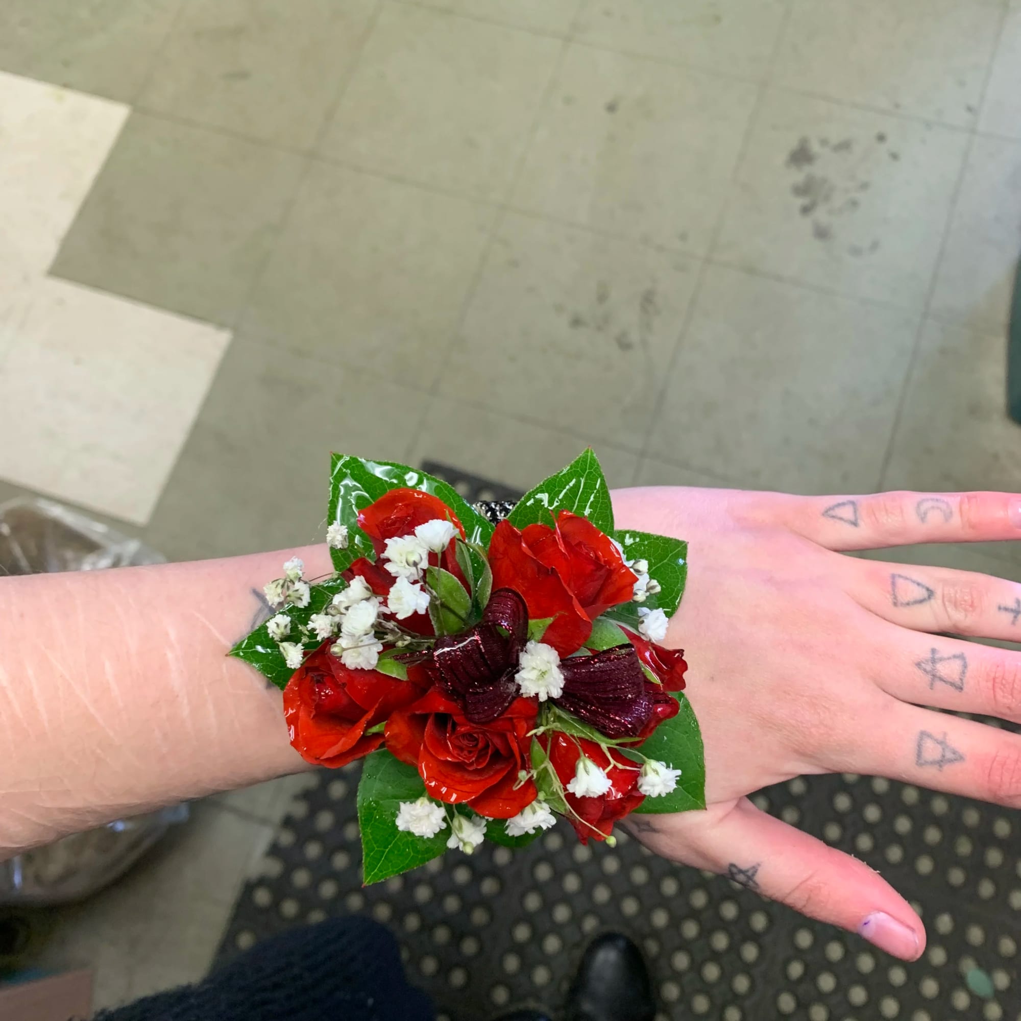 Red floral wrist corsage with white filler flowers on a hand