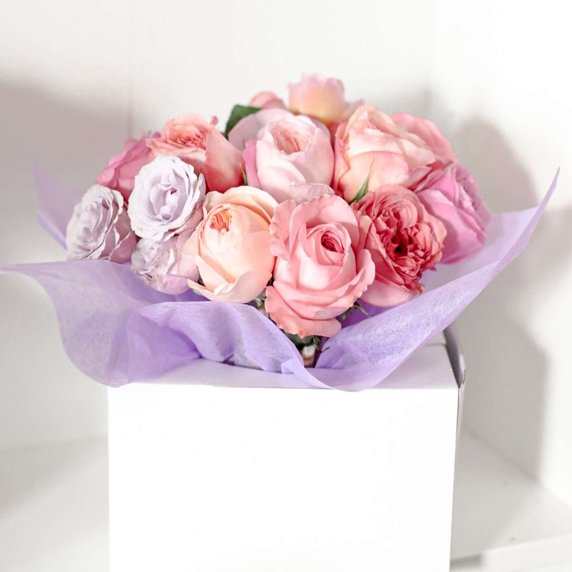 Pink and peach roses wrapped in lavender paper on a white box