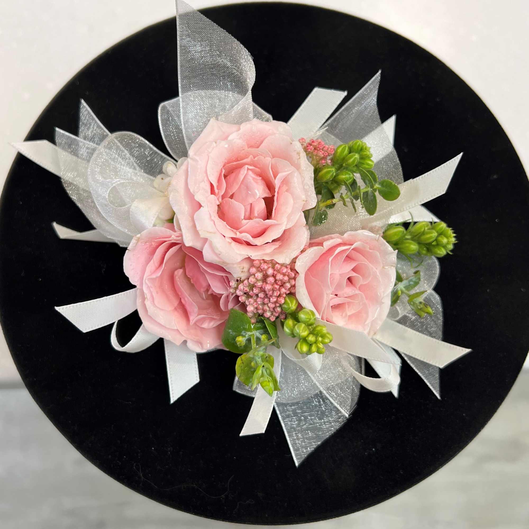 Pink rose corsage with white ribbon on a black round base