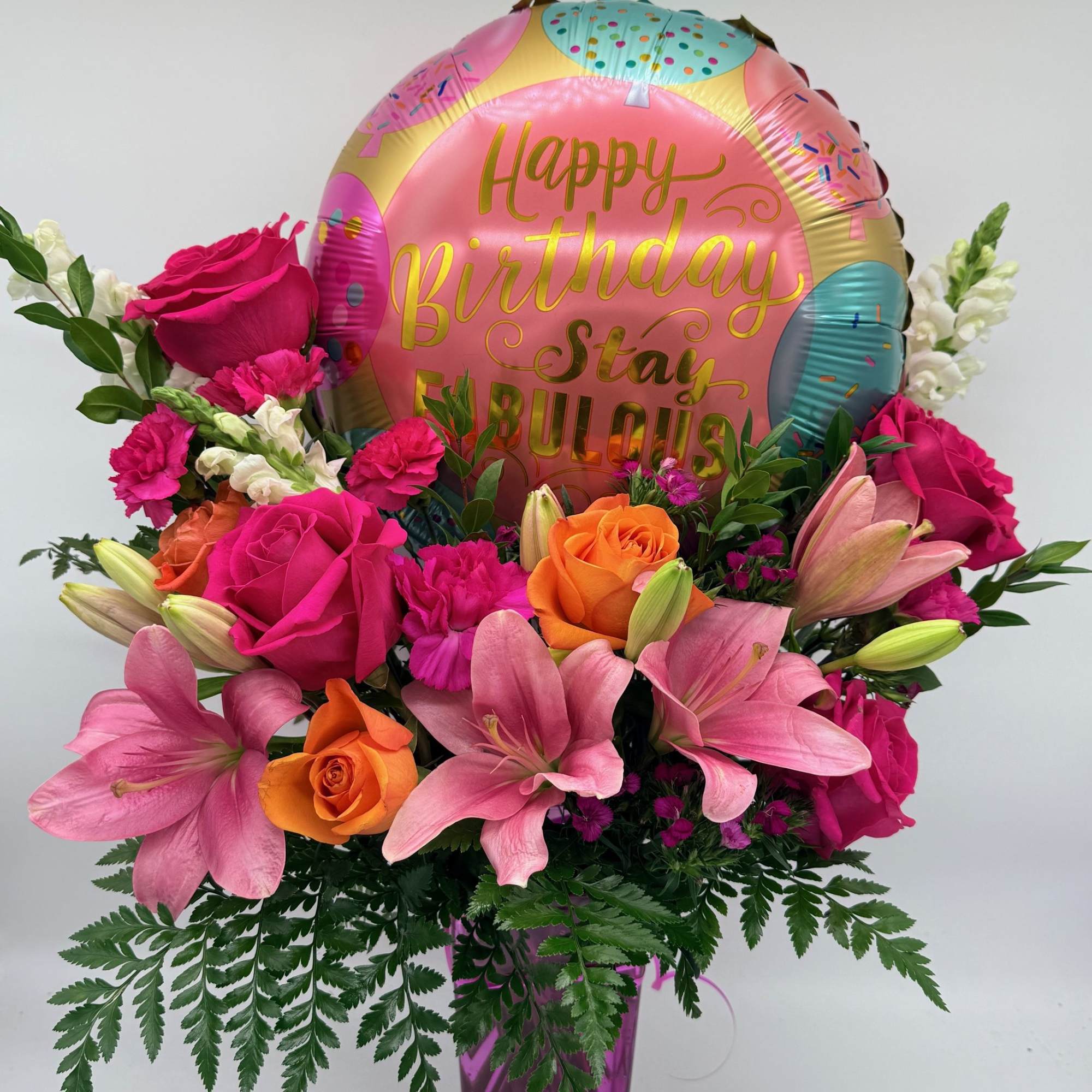 Birthday bouquet with roses, lilies, and a foil balloon in a purple vase