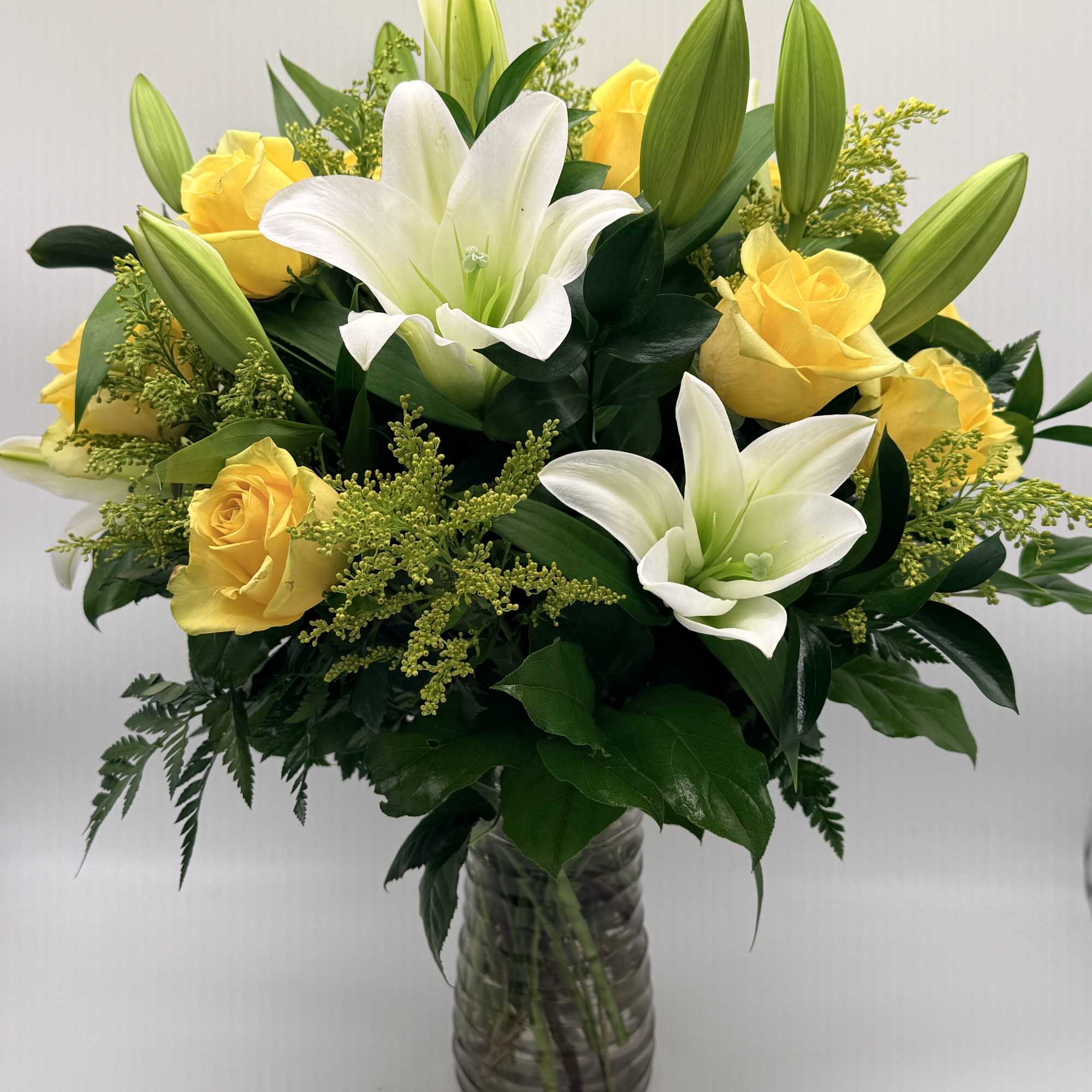 Yellow roses and white lilies arranged in a glass vase