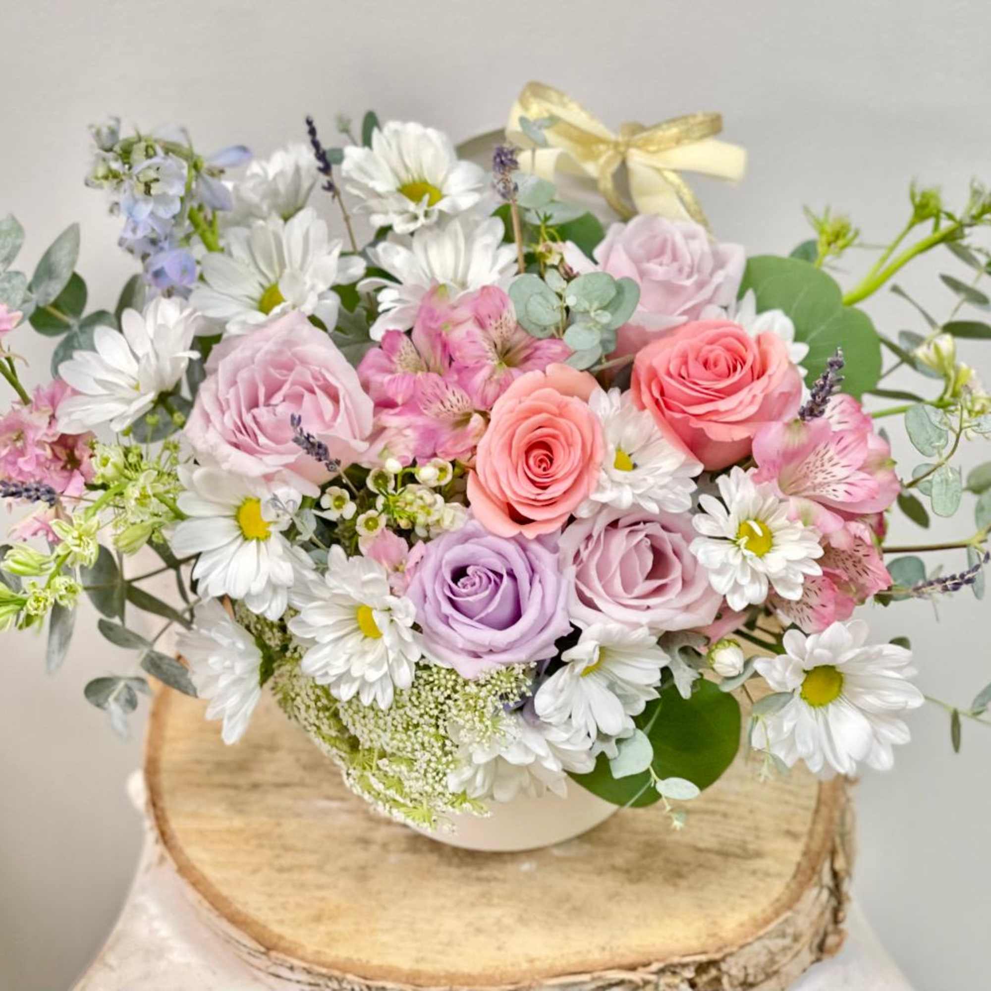 Pastel bouquet of roses and daisies in a white container with a ribbon