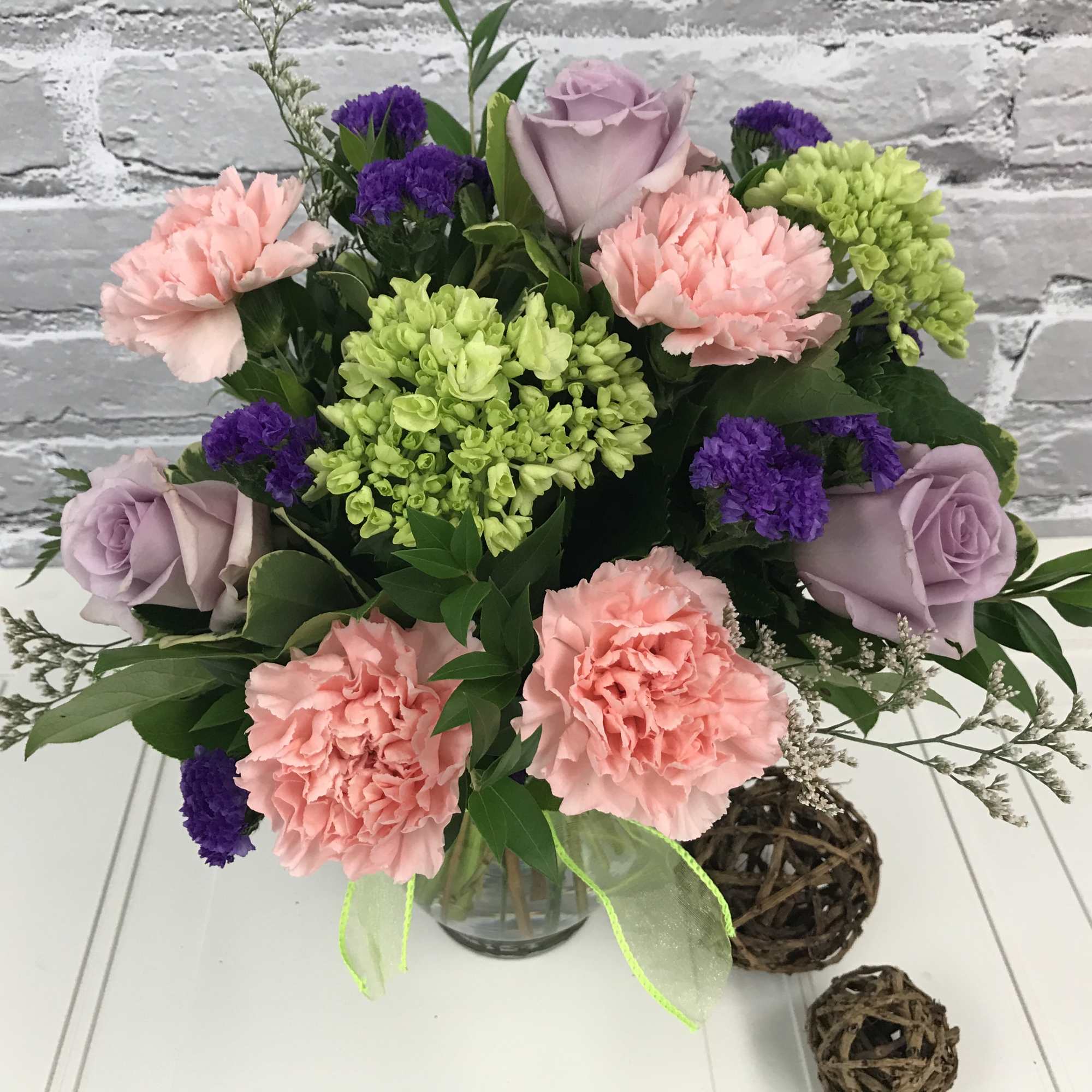 Bouquet of pink carnations, lavender roses, and green hydrangeas in a glass vase