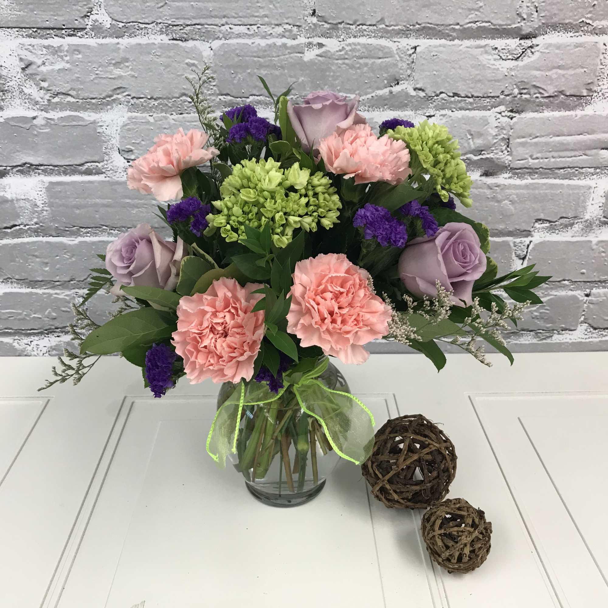 Bouquet of pink carnations, lavender roses, and green blooms in a glass vase