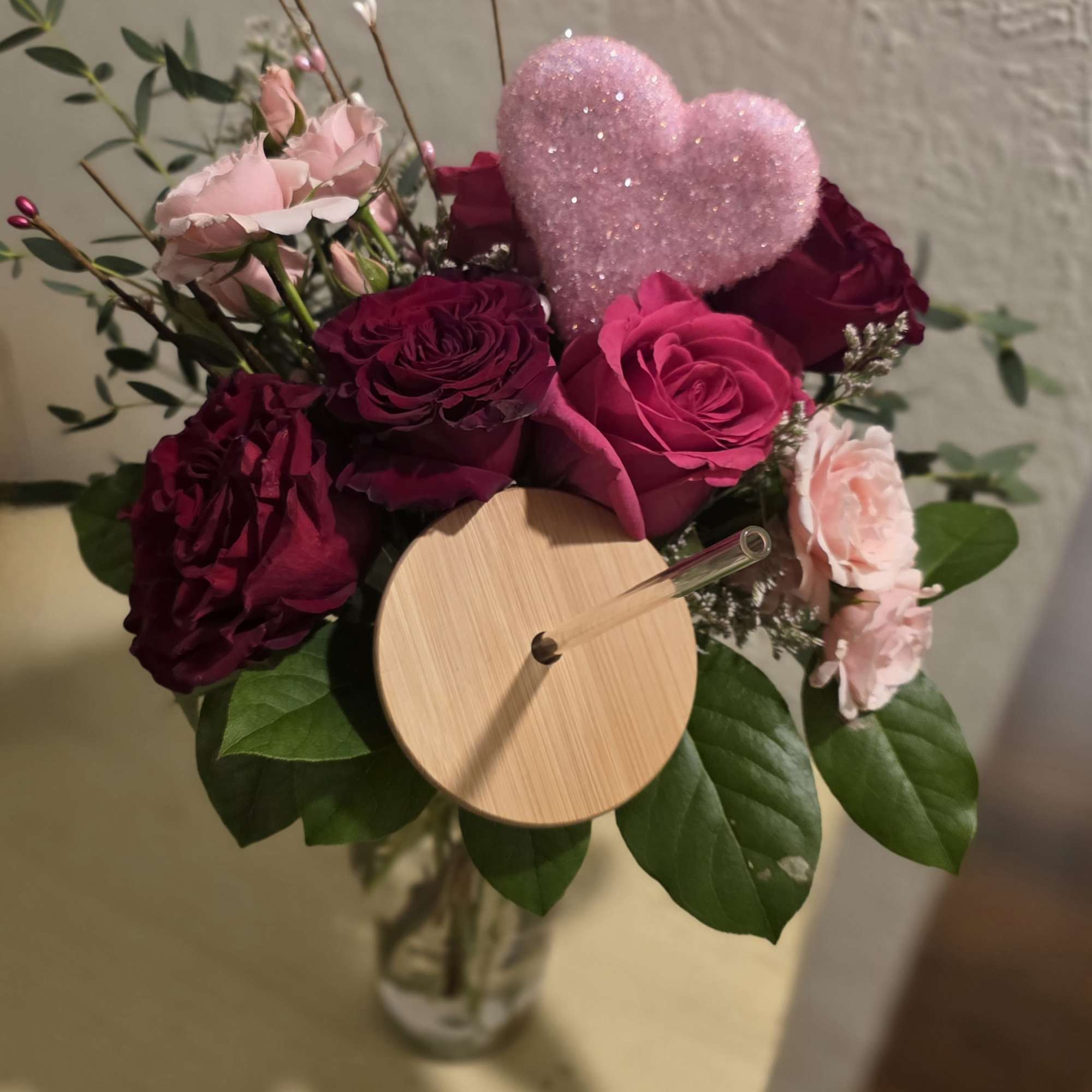 Pink and burgundy roses in a glass vase with a glittery heart pick