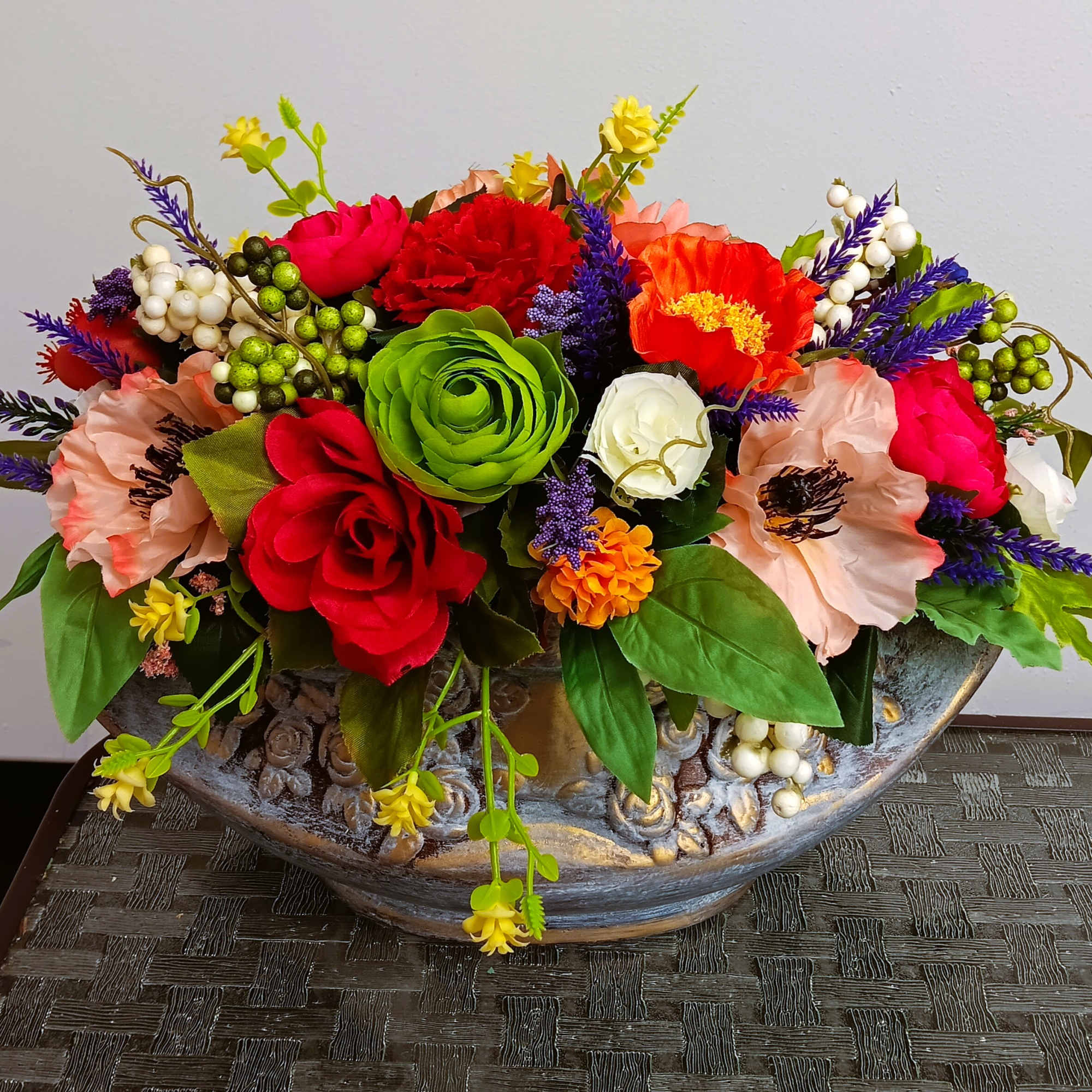 Colorful floral arrangement in a decorative bowl with red, pink, orange, and green blooms