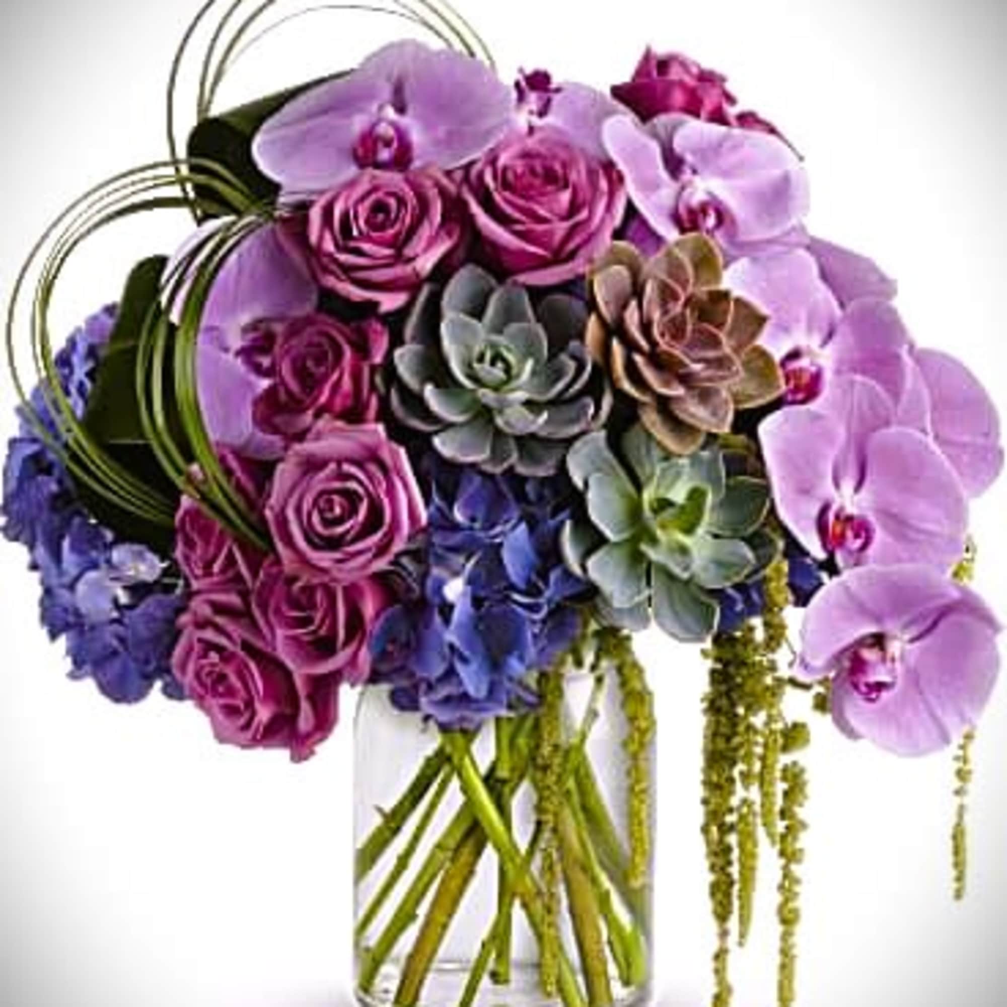 Bouquet of purple orchids, roses, and succulents in a clear glass vase
