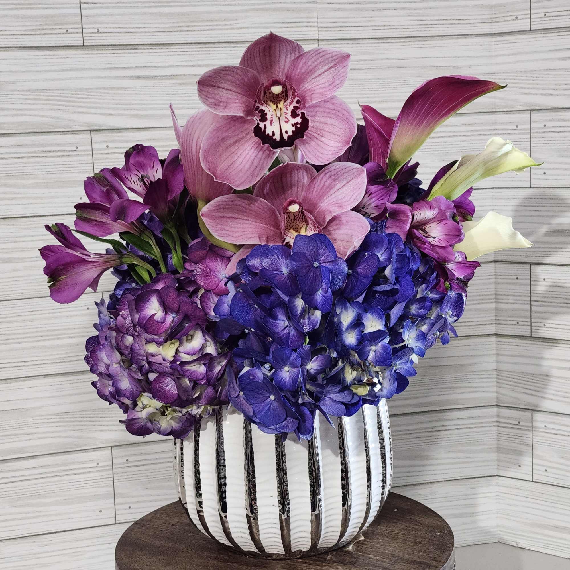 Purple orchid and hydrangea arrangement in a striped vase