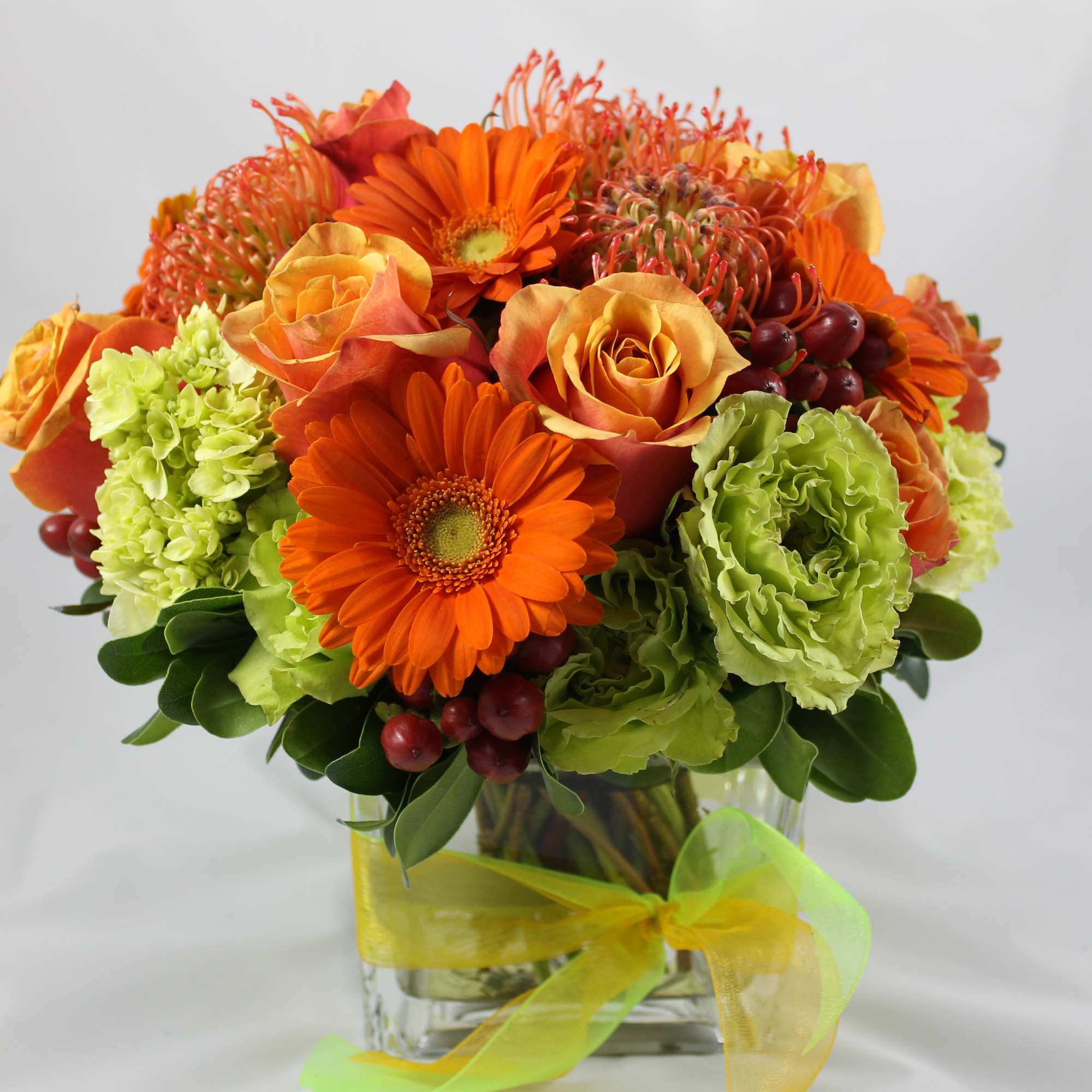 Orange and green floral arrangement in a clear glass vase with a yellow ribbon