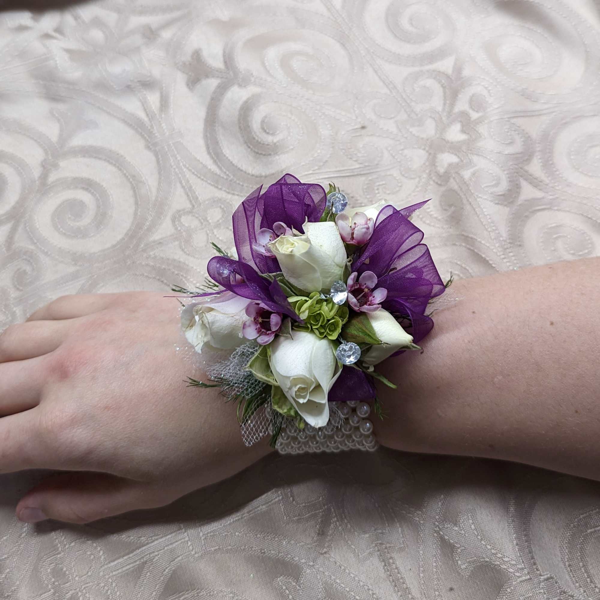 Wrist corsage with white roses and purple ribbon on a hand