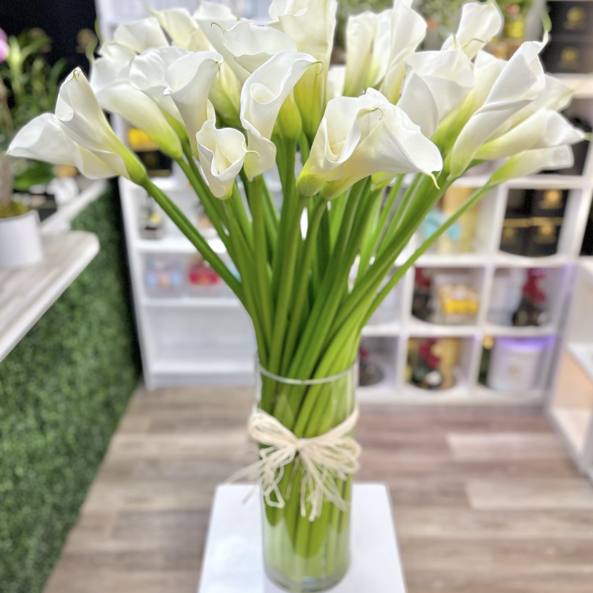 Tall glass vase filled with white calla lilies tied with a raffia bow