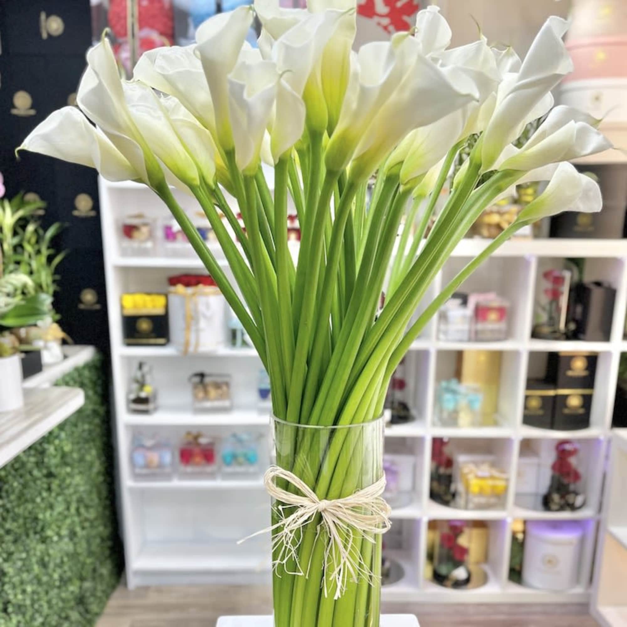 Tall bundle of white calla lilies in a clear glass vase tied with raffia