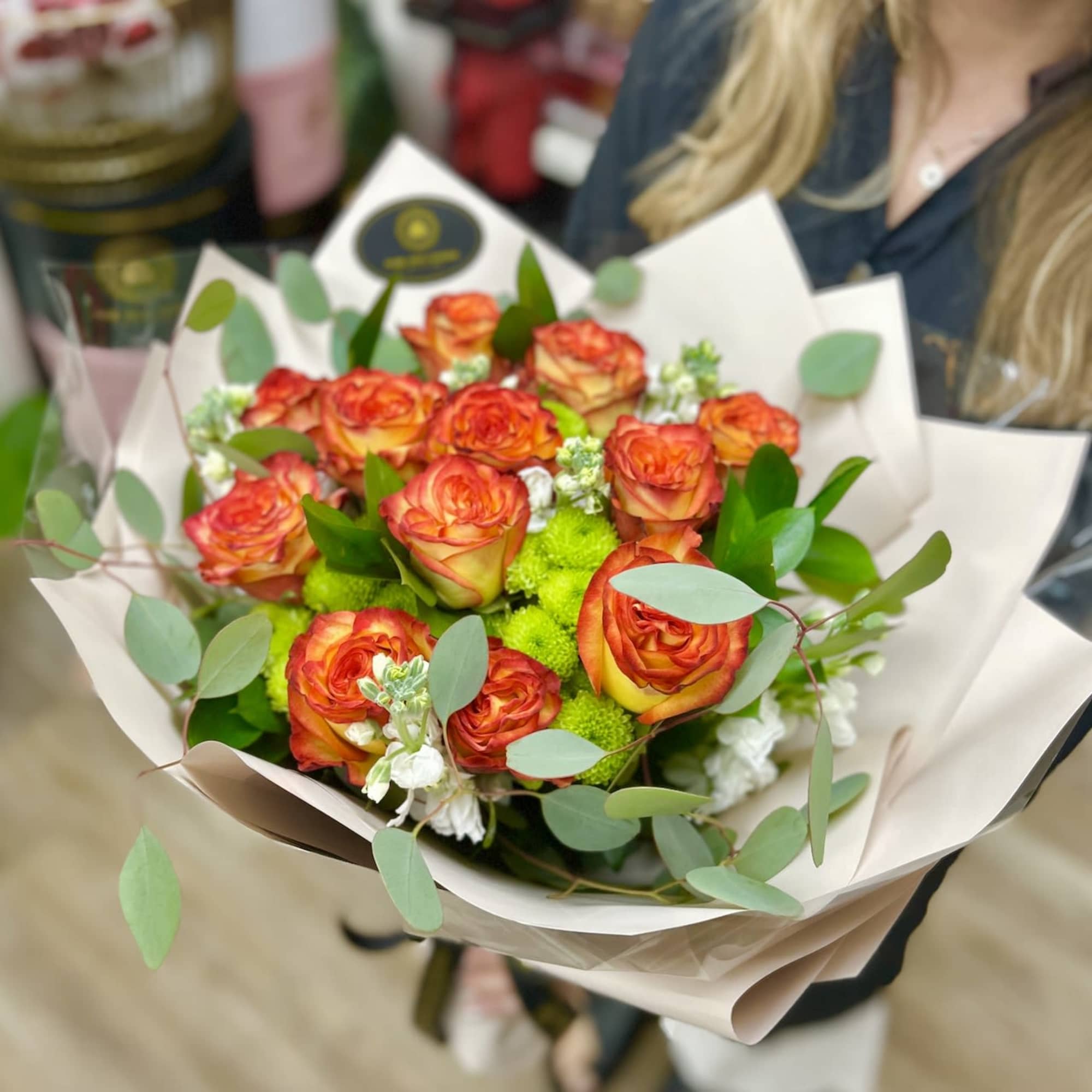 Bouquet of orange-yellow roses with green and white flowers wrapped in pale paper