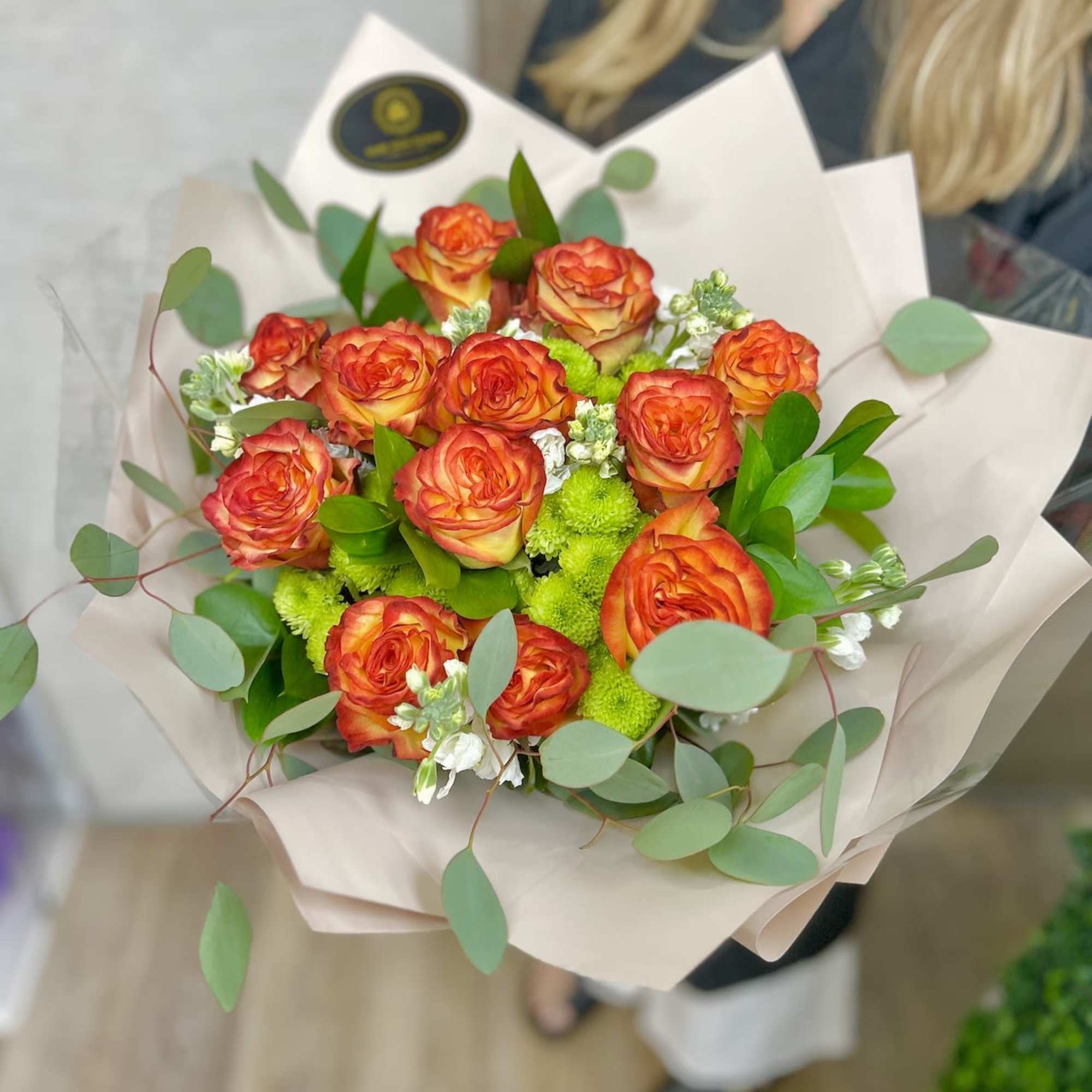 Hand-tied bouquet of orange roses with green accents wrapped in beige paper