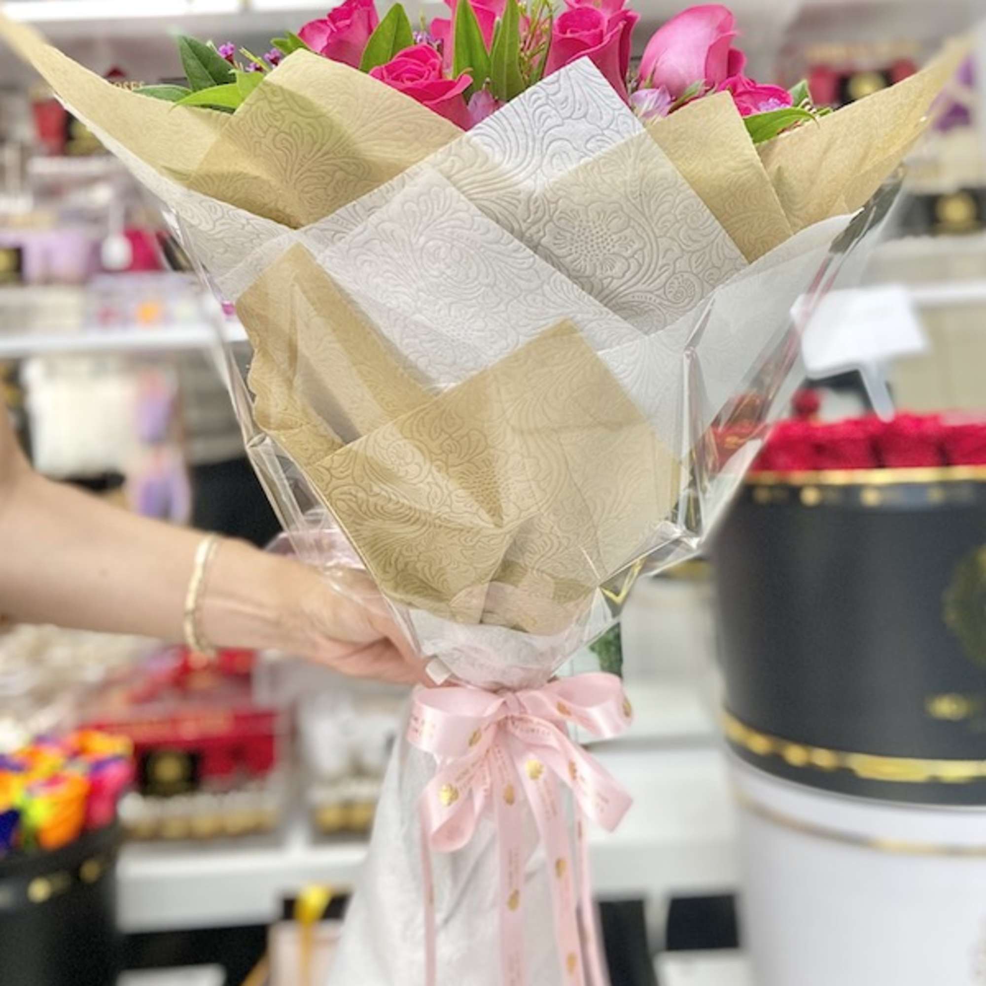 Handheld bouquet of bright pink roses wrapped in patterned paper and tied with a pink ribbon.