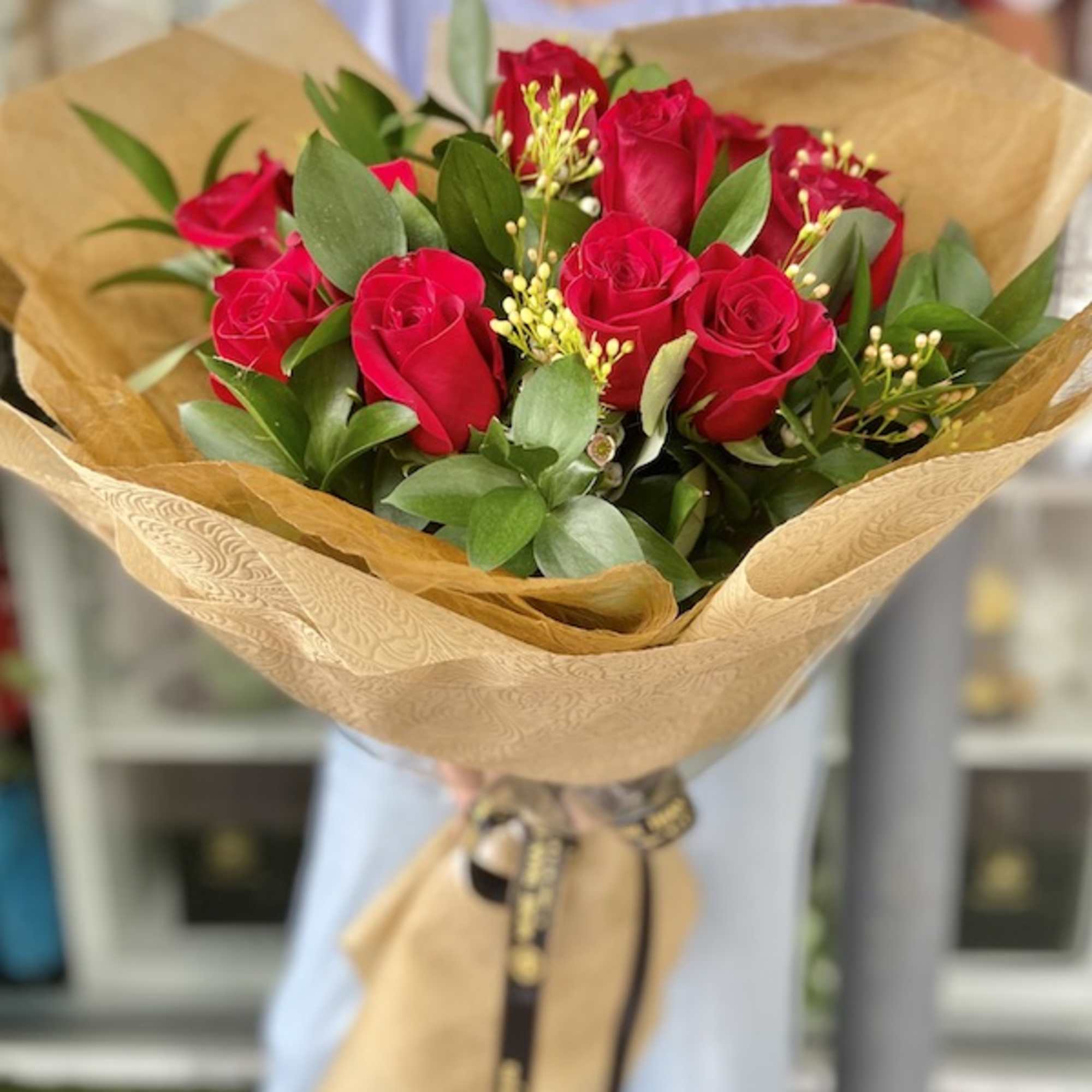 Hand-tied bouquet of red roses wrapped in tan paper and tied with a printed ribbon