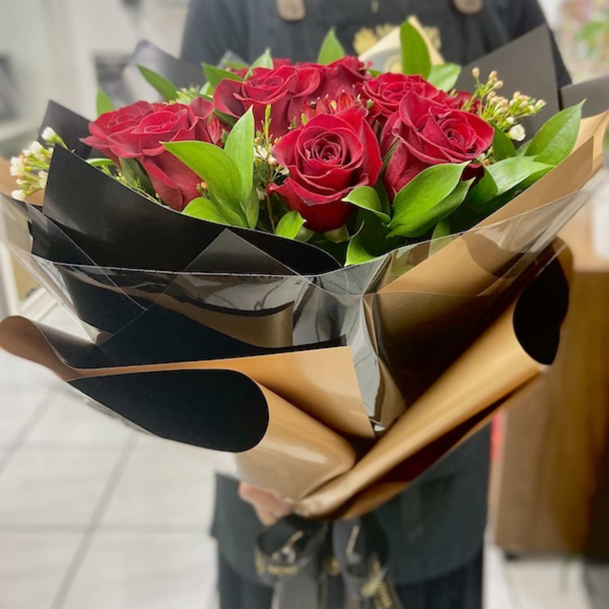 Hand-tied bouquet of red roses with foliage wrapped in black and gold paper