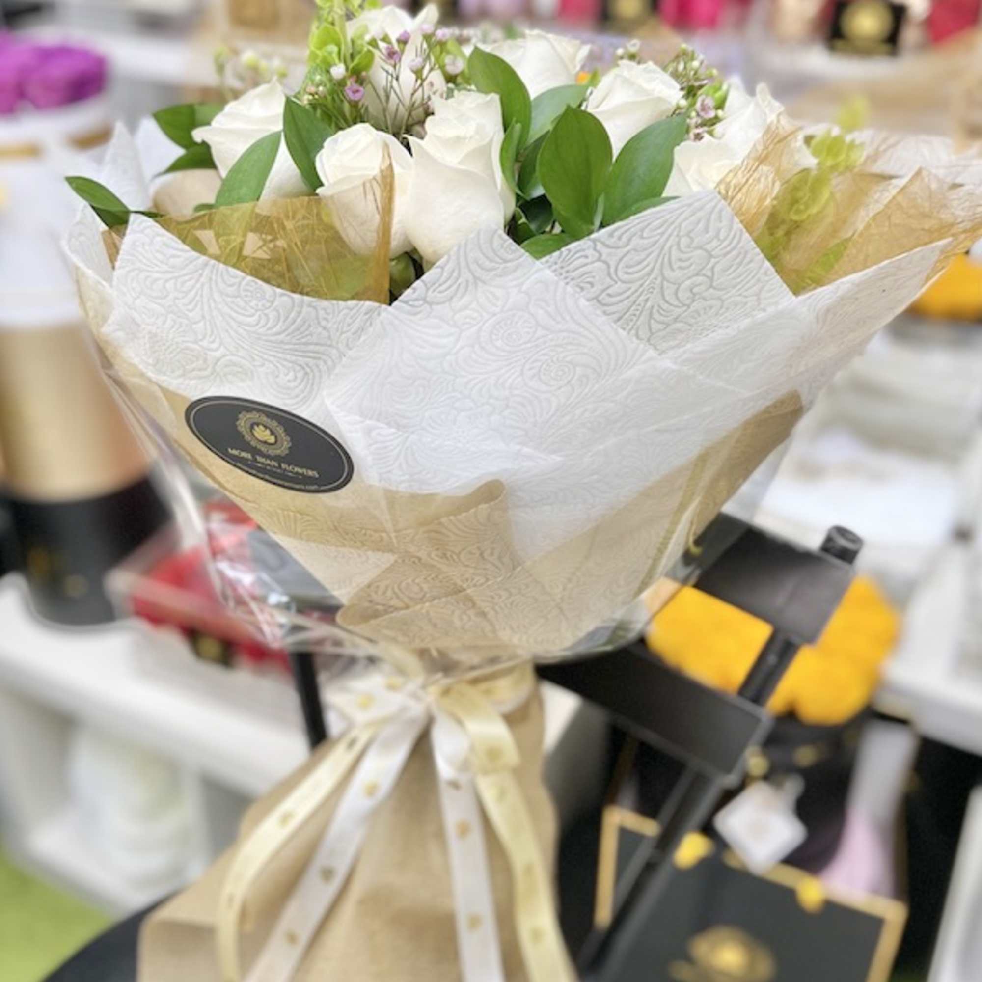 Hand-tied bouquet of white roses wrapped in patterned paper and ribbon