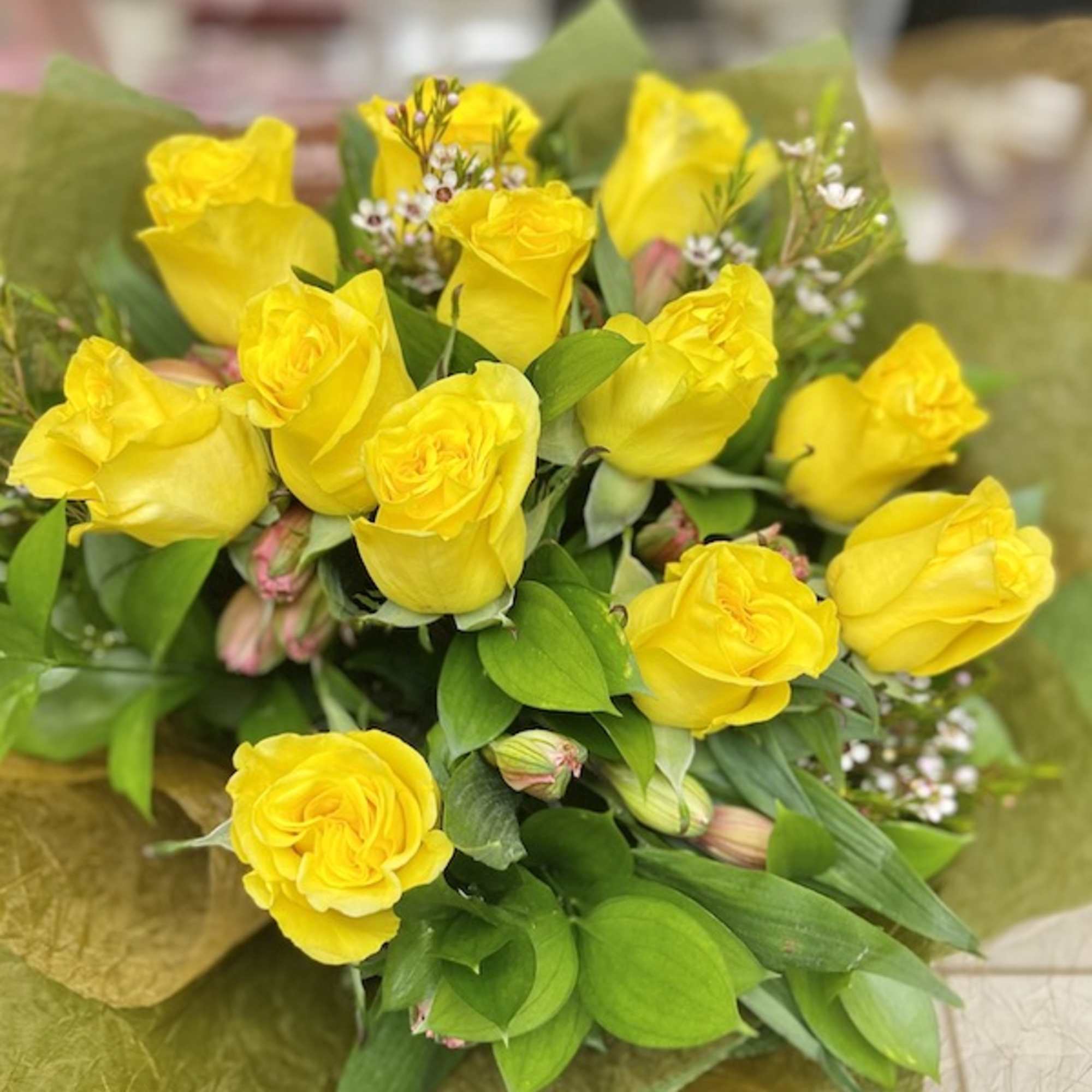 Bouquet of bright yellow roses with small white filler flowers wrapped in green tissue paper