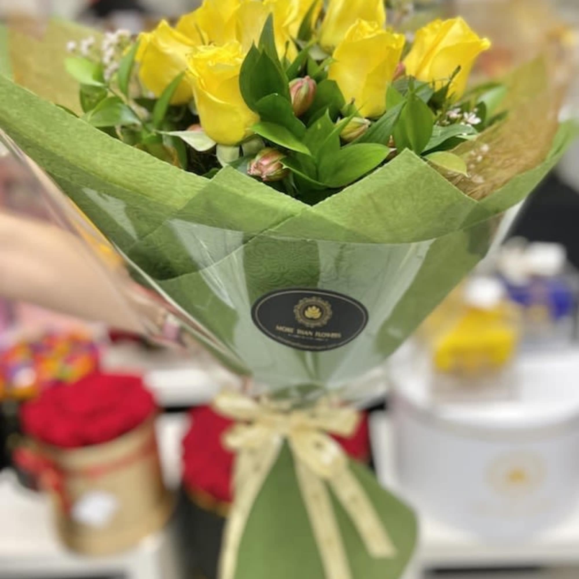 Handheld bouquet of yellow roses wrapped in green paper with a cream ribbon bow