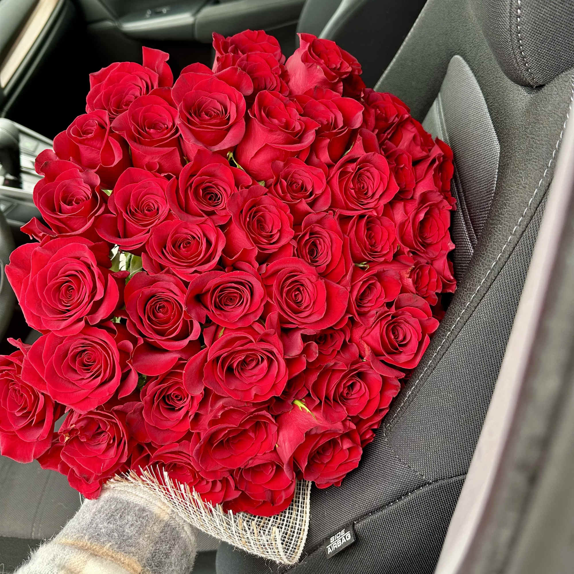 Large bouquet of tightly clustered red roses resting on a car seat