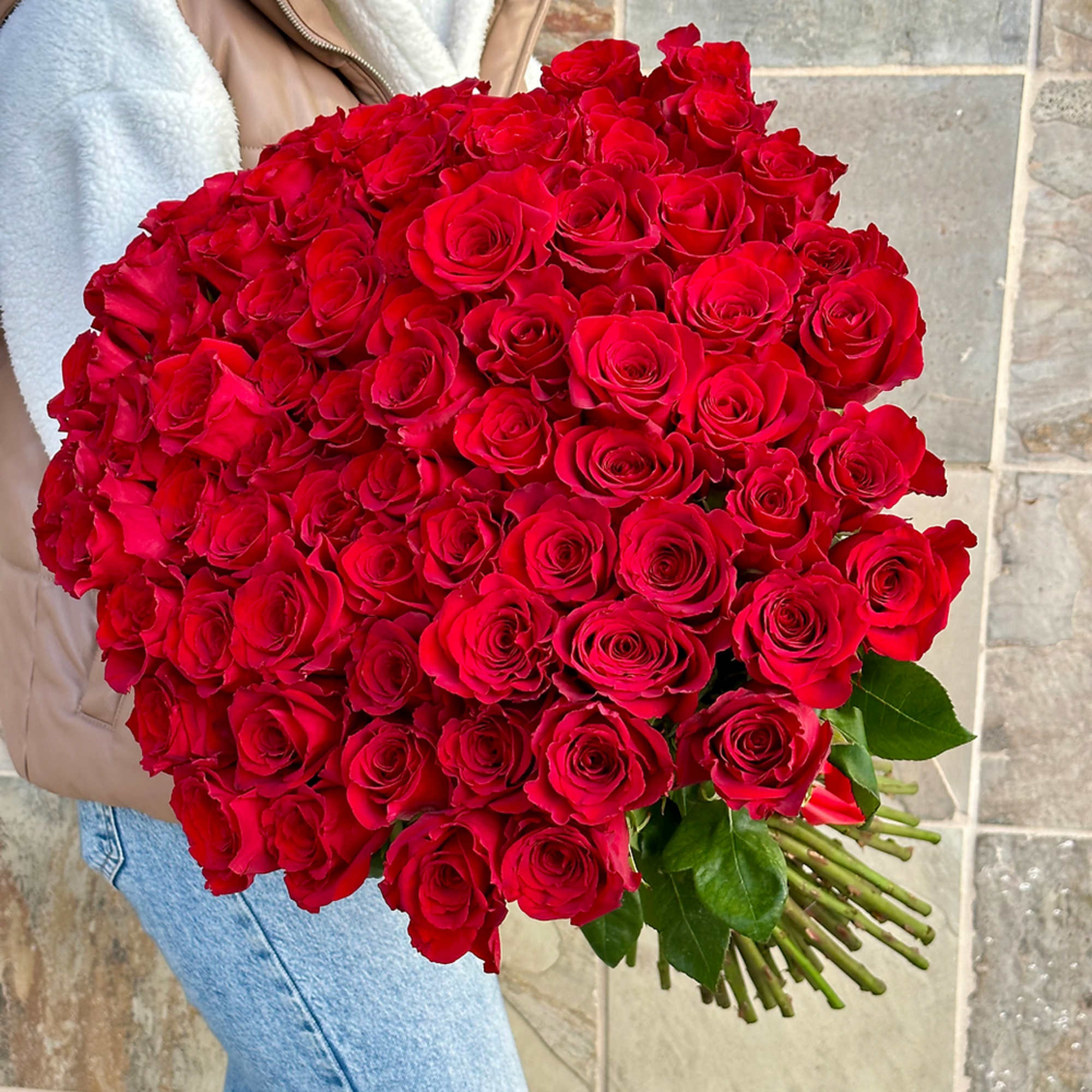 Oversized bouquet of tightly clustered red roses held in someone's arms