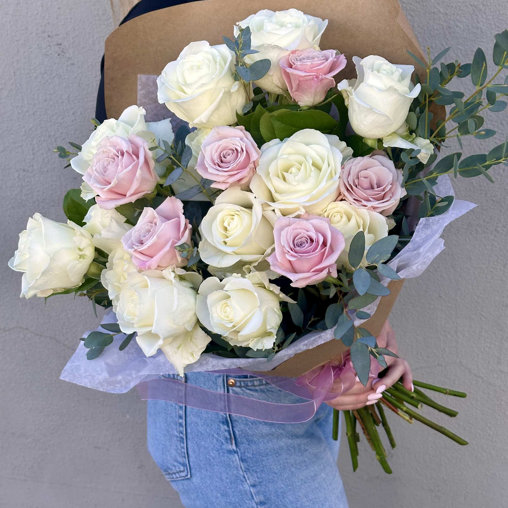 Large hand-tied bouquet of white and pale pink roses wrapped in kraft paper, held by a person.