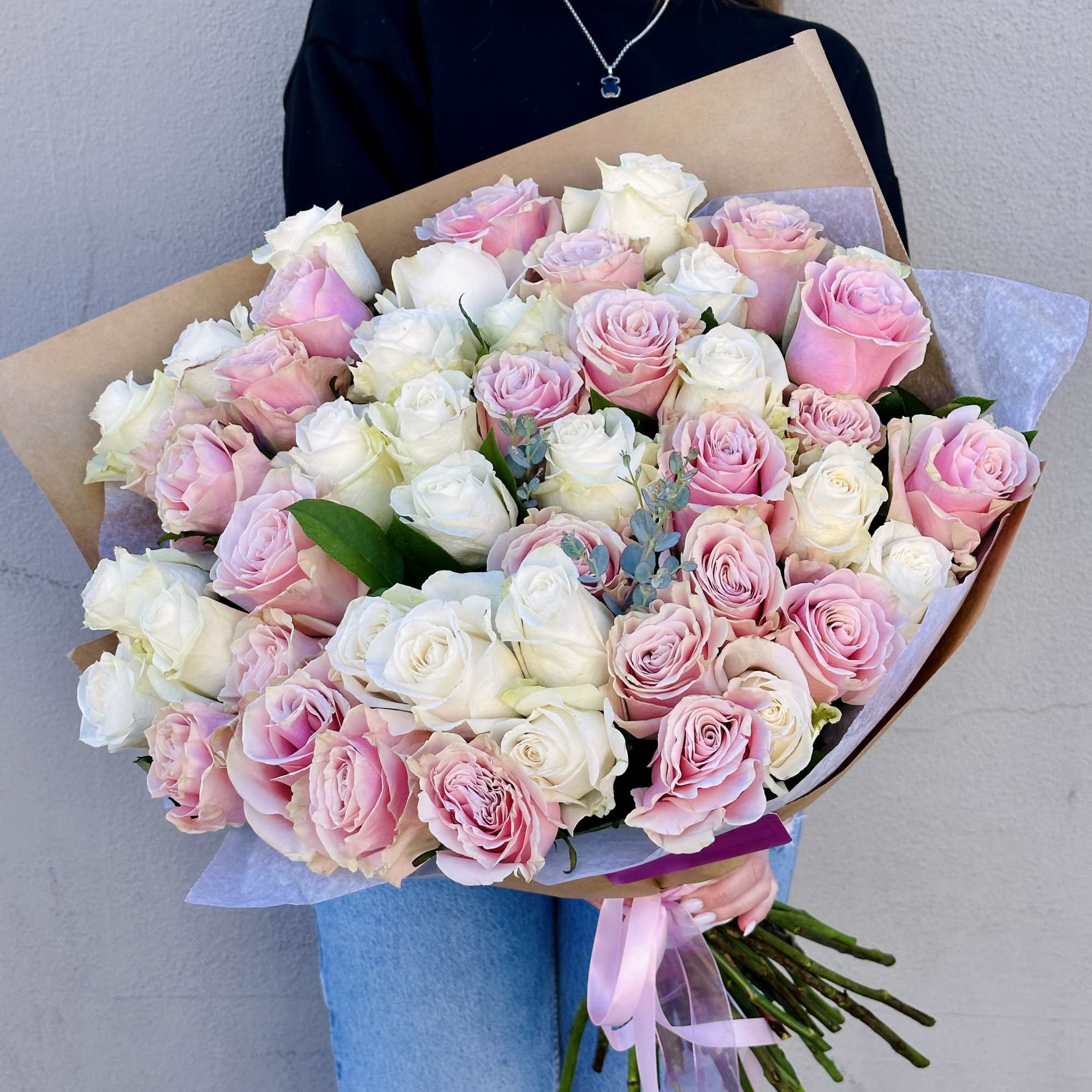 Large hand-tied bouquet of white and pink roses wrapped in kraft paper and tied with pink ribbon