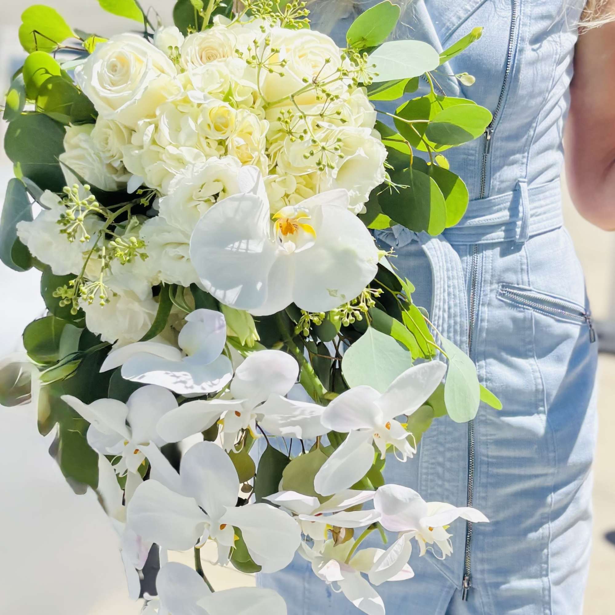 White bouquet with roses and orchids held by a person in a light blue dress