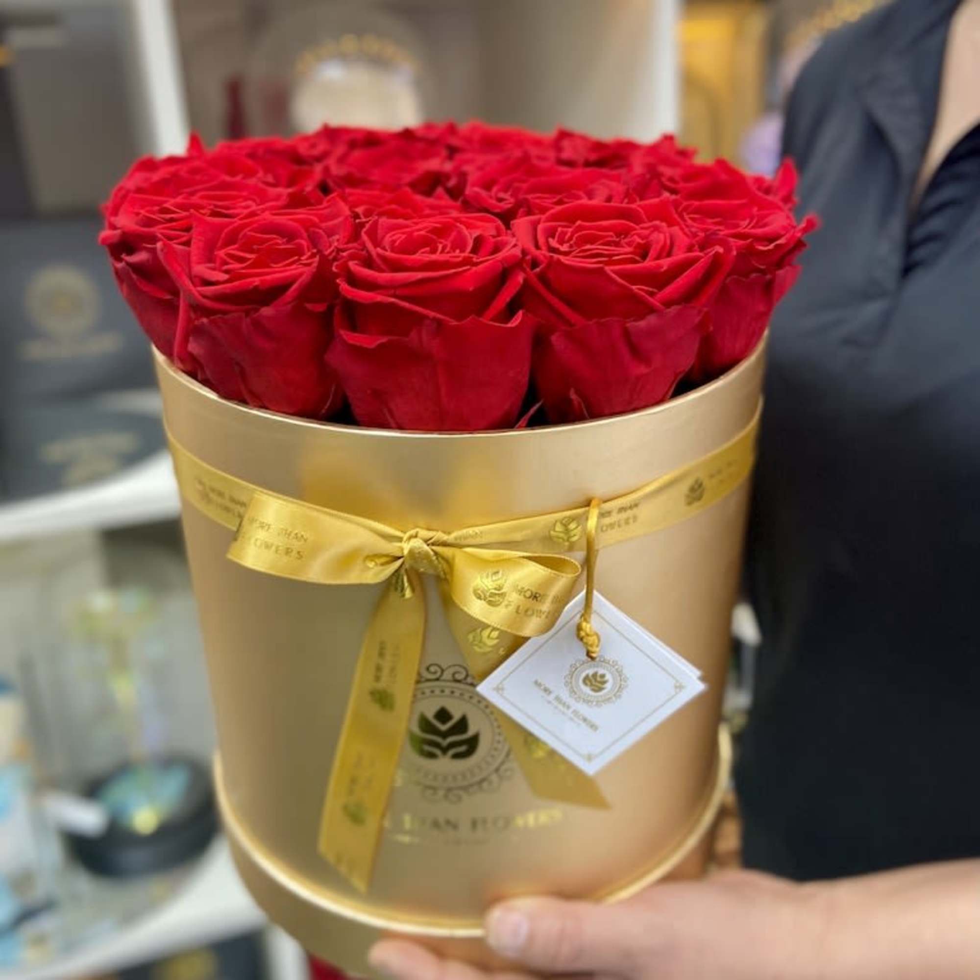 Round gold hatbox filled with red roses, tied with a yellow ribbon and gift tag