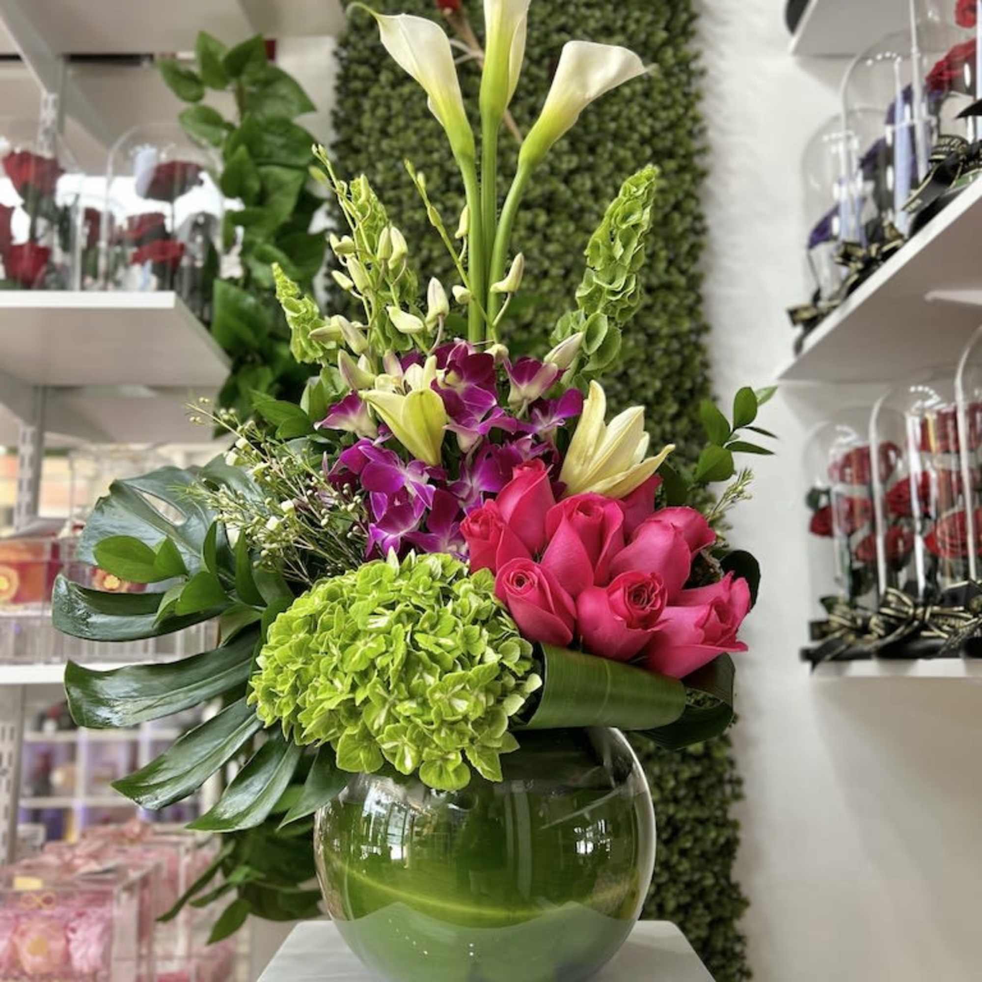 Tall mixed arrangement with white calla lilies, pink roses, orchids and green hydrangea in a round glass vase