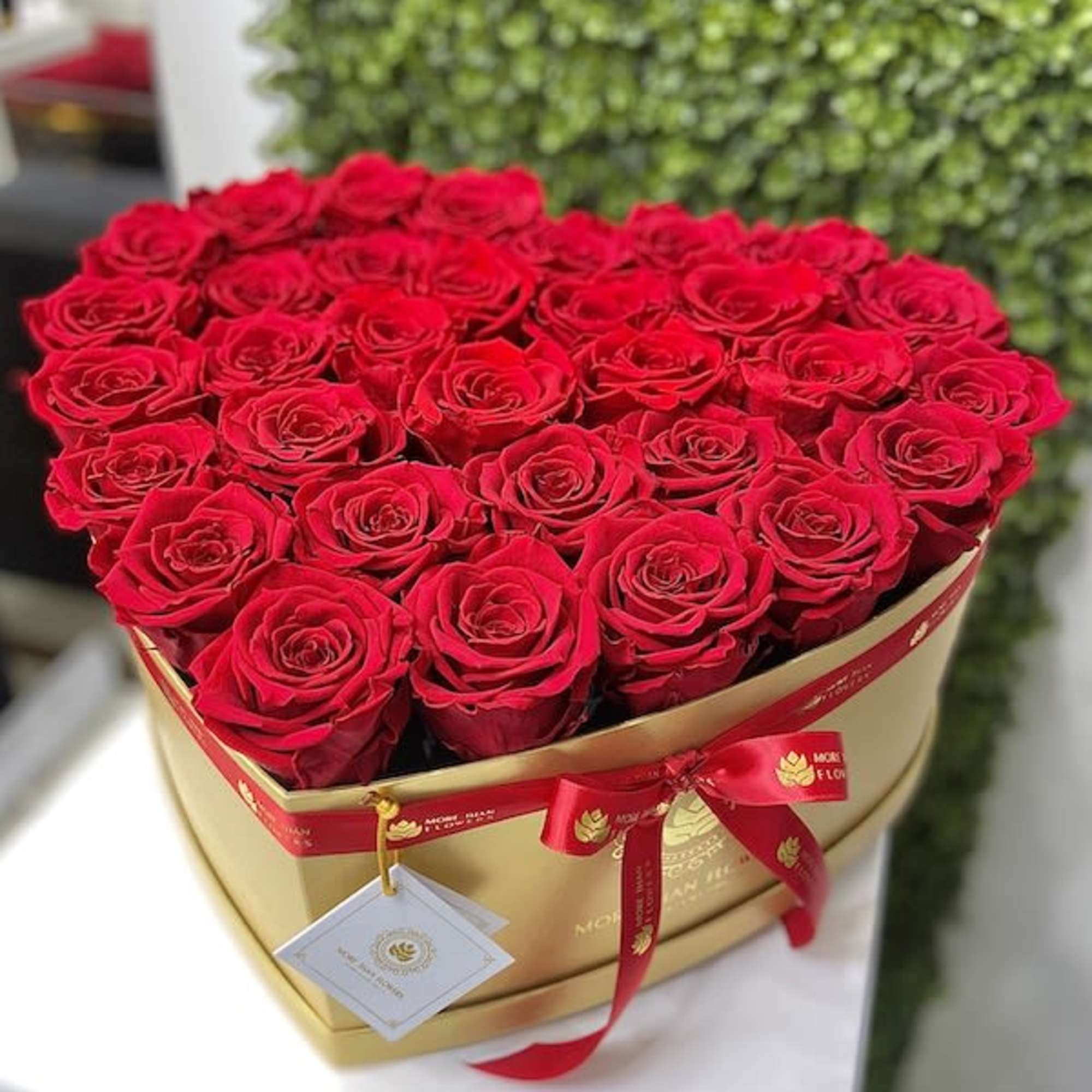 Heart-shaped gold box filled with red roses and tied with a red ribbon and tag