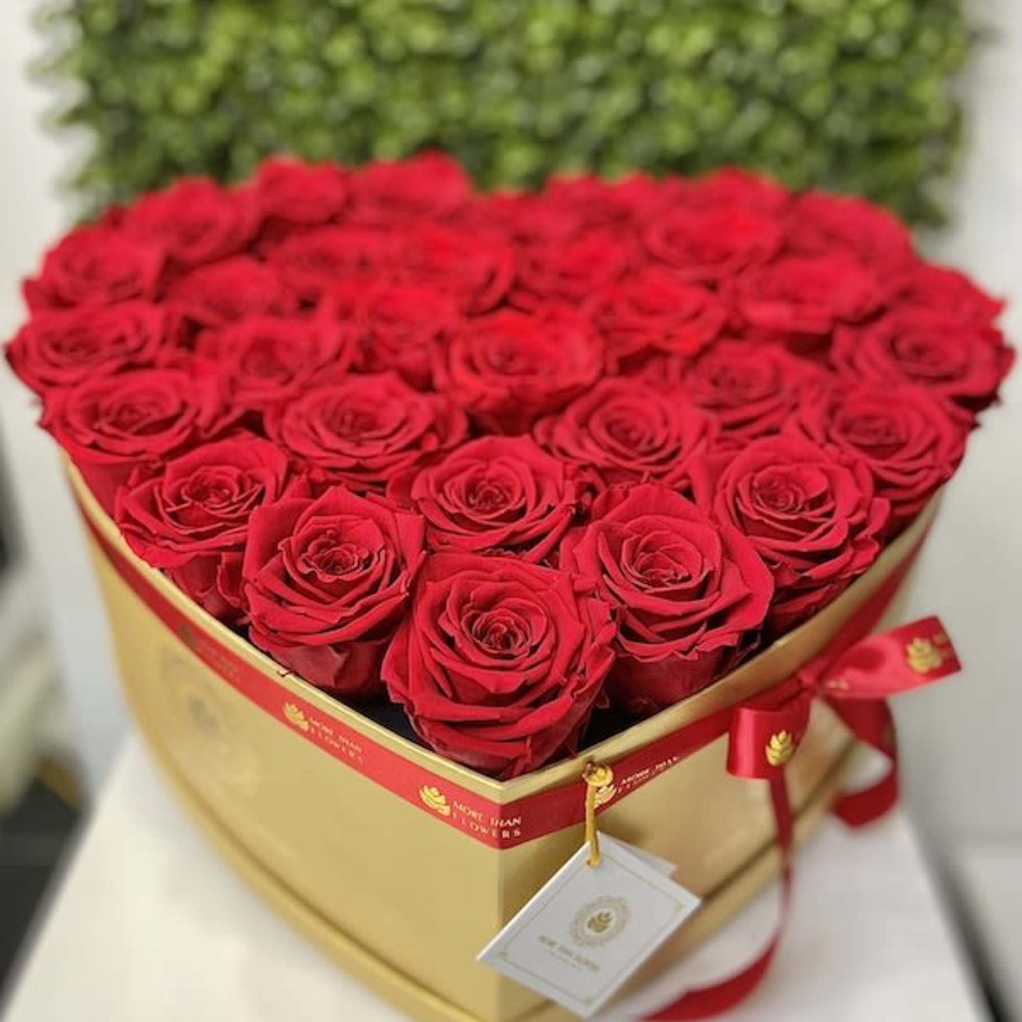 Heart-shaped gold box filled with tightly packed red roses and tied with a red ribbon.