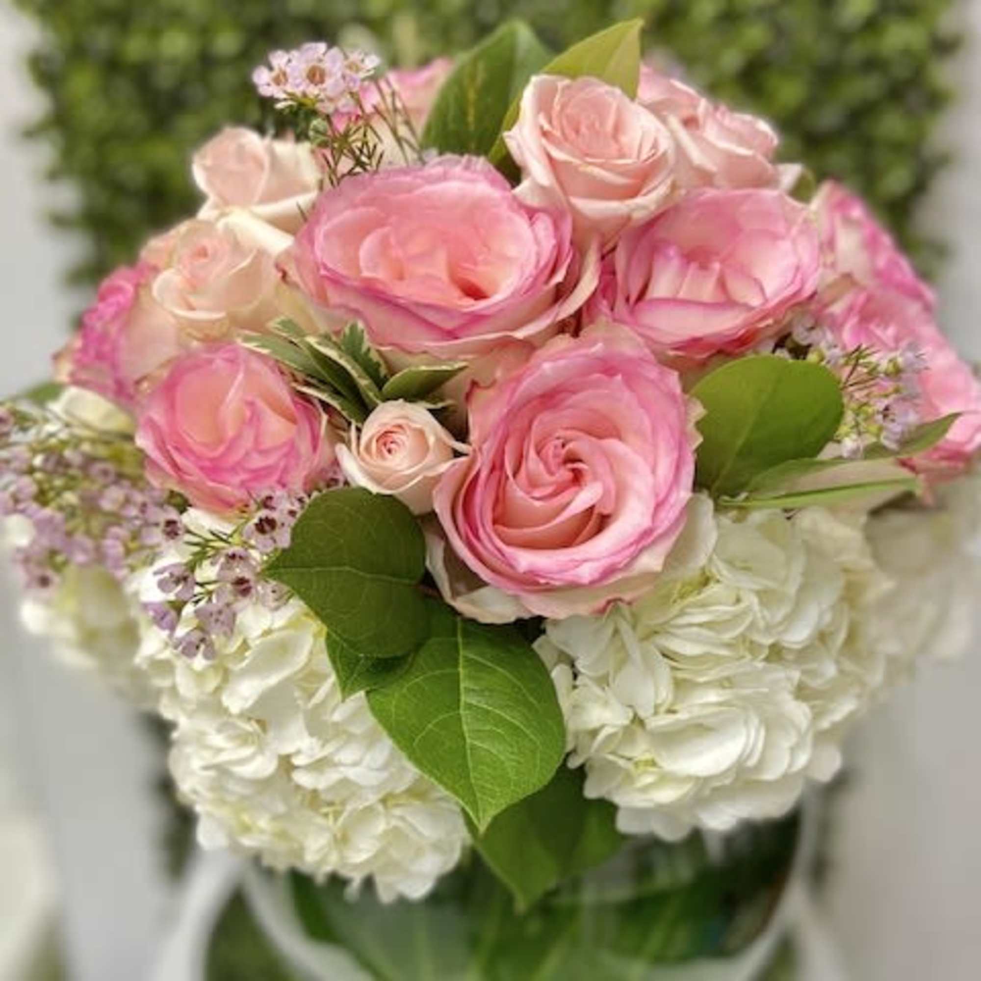 Round arrangement of pink roses and small pink blooms over white hydrangeas in a clear glass vase