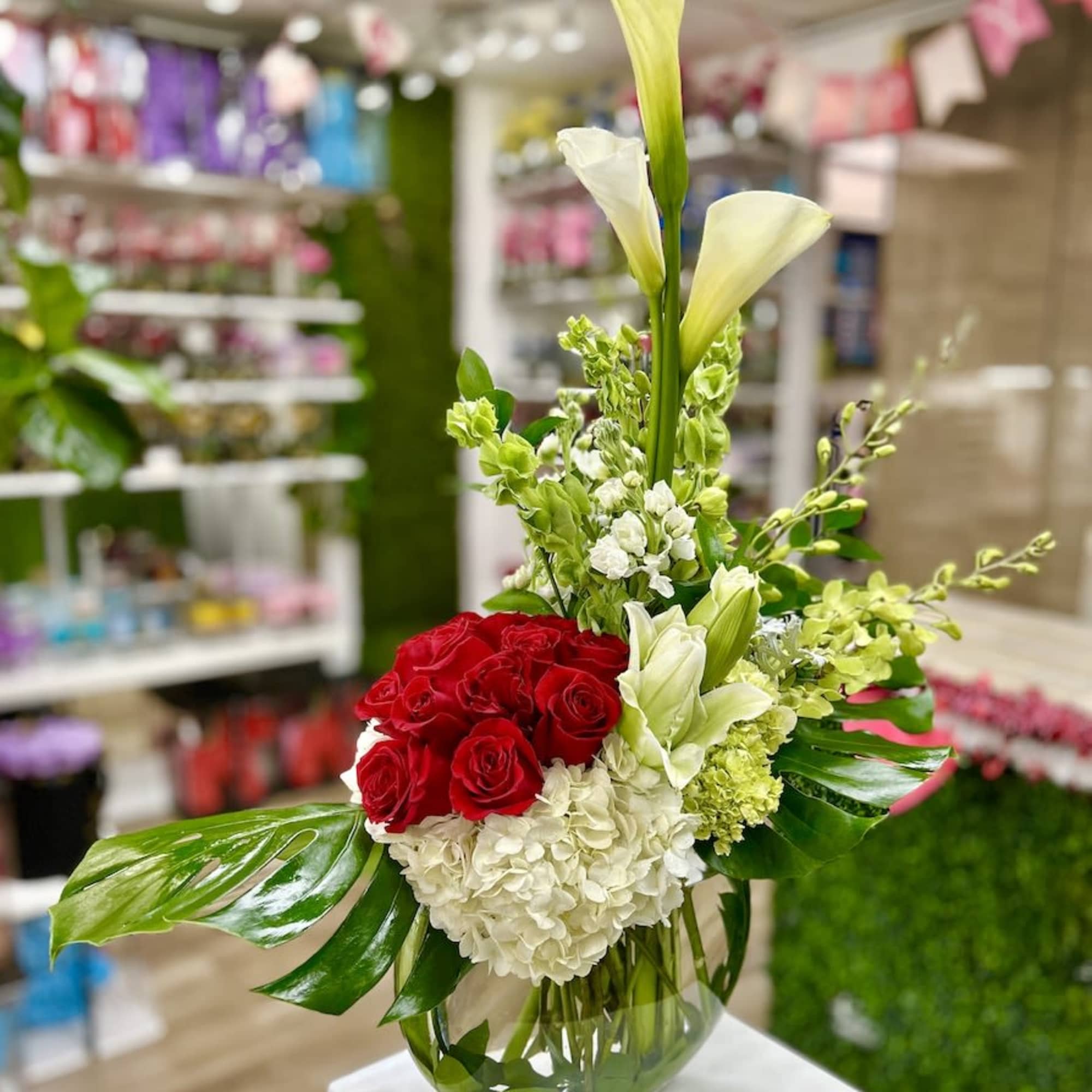 Tall arrangement of white calla lilies, red roses, and white hydrangeas in a clear glass vase
