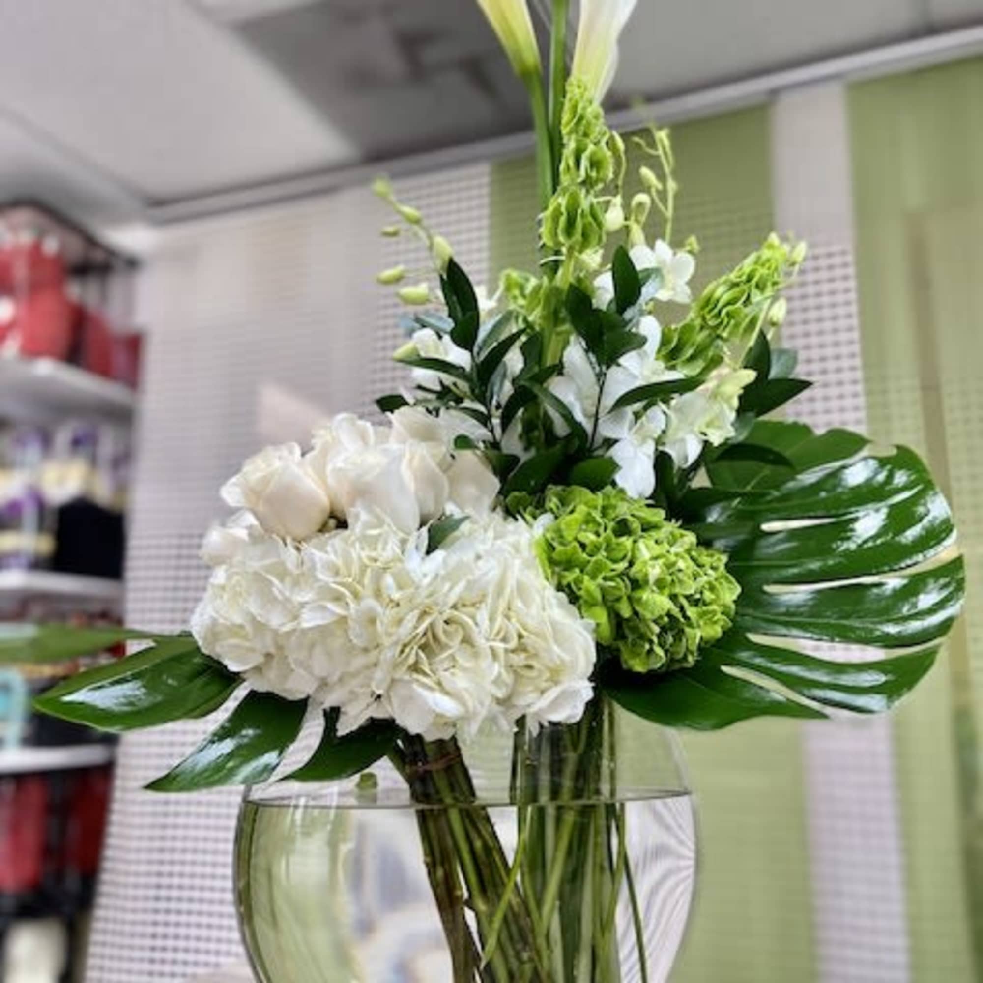 Modern white and green arrangement with calla lilies and hydrangeas in a round glass vase