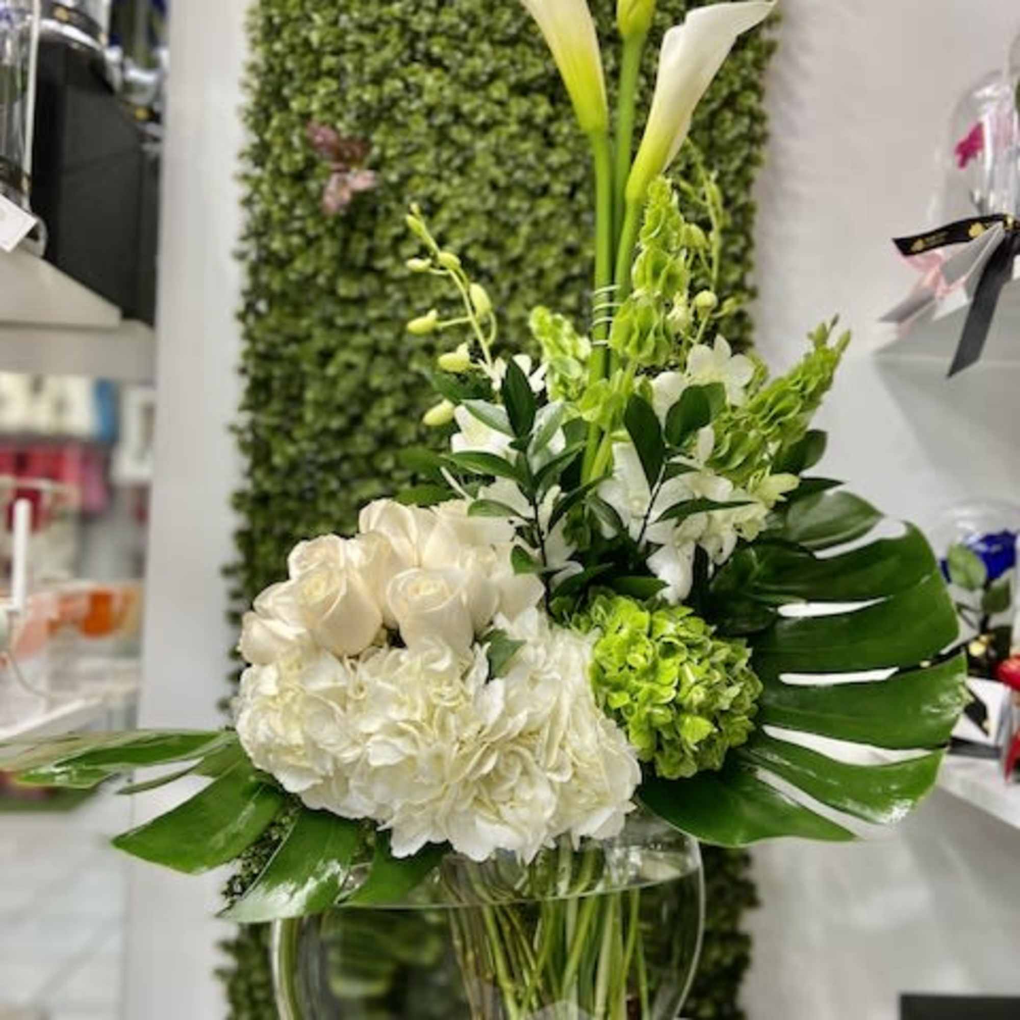 White and green floral arrangement with tall calla lilies in a round glass bowl vase