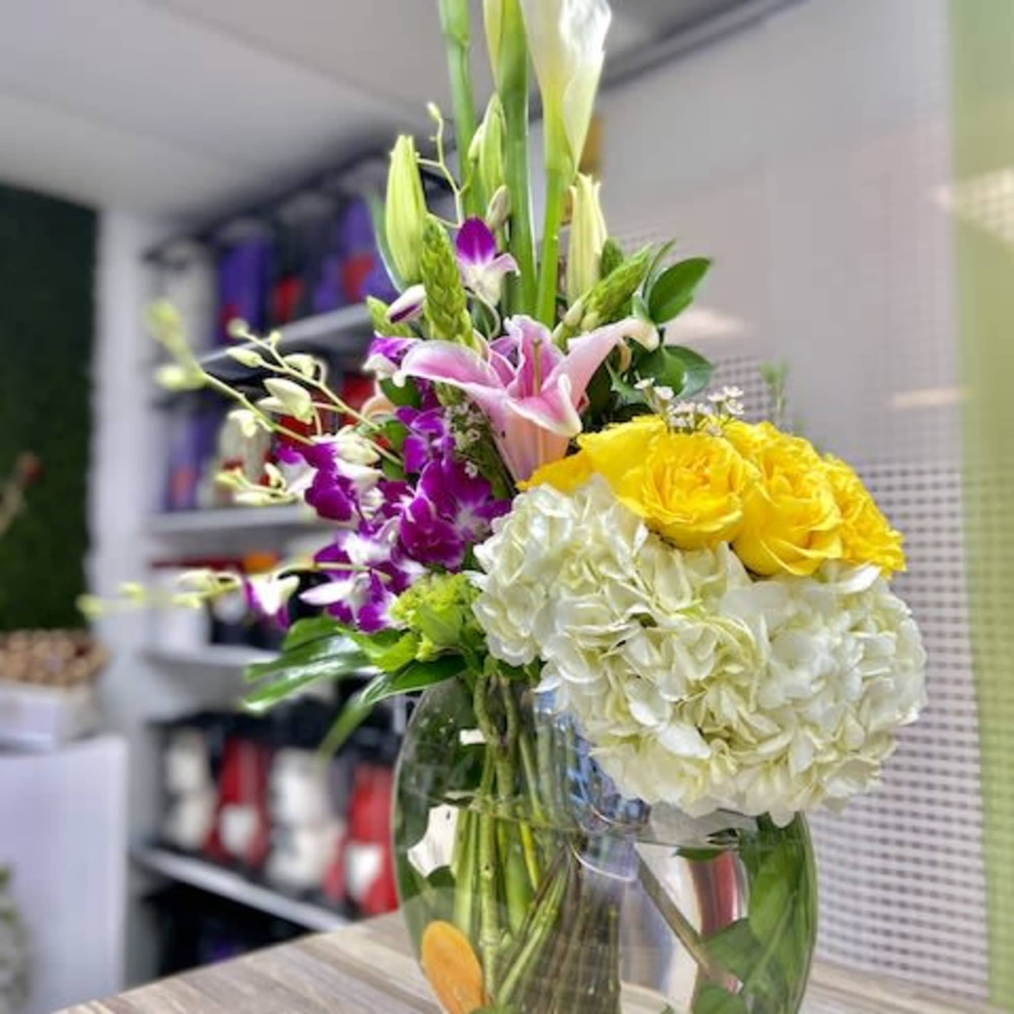 Tall mixed arrangement with white calla lilies, purple orchids, yellow roses and white hydrangeas in a clear round vase