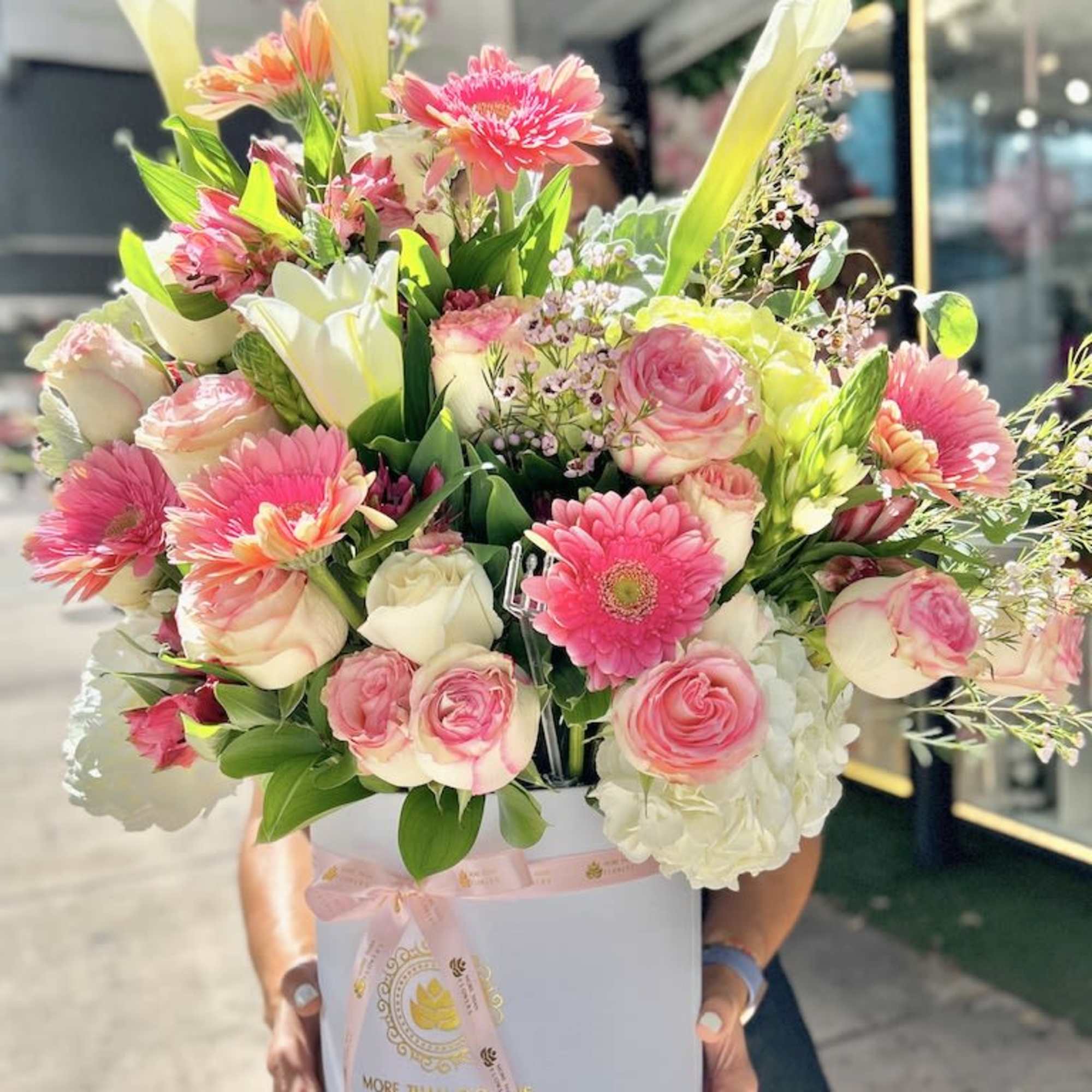 Large pink and white flower arrangement with gerberas, roses, and calla lilies in a round hatbox.