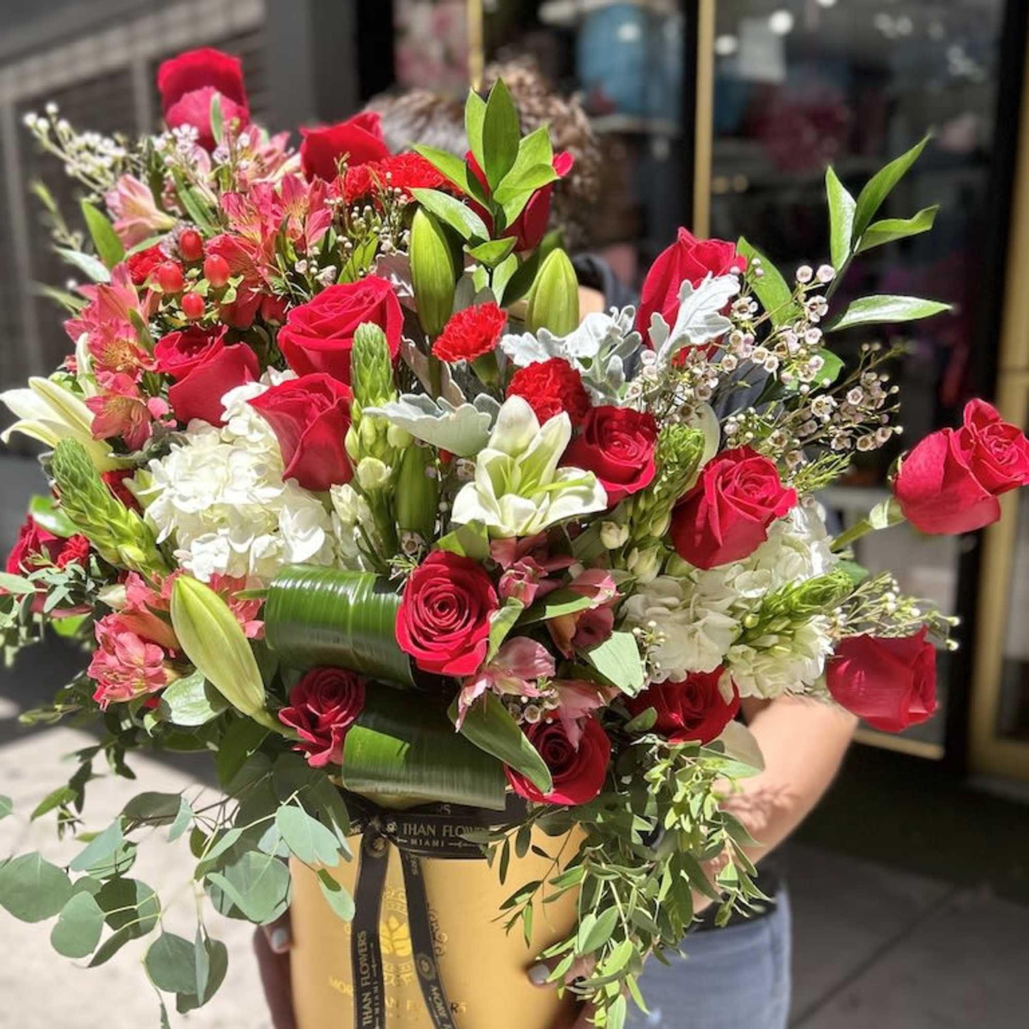 Tall red and white flower arrangement with roses and lilies in a gold hatbox-style container