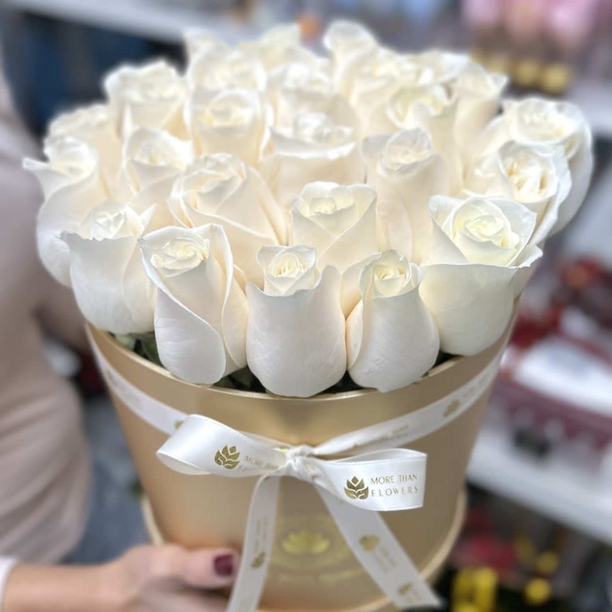 Round gold box filled with white roses and tied with a white ribbon.